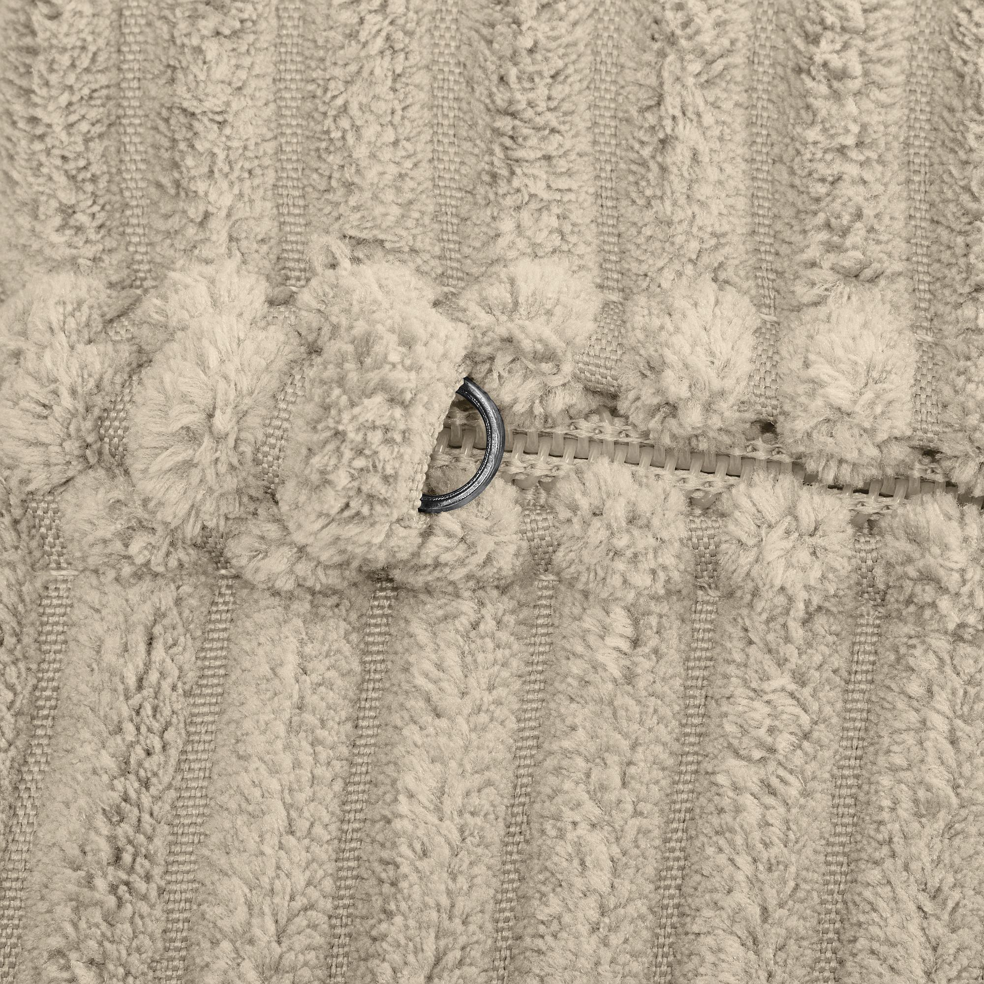 Nahaufnahme eines beigefarbenen strukturierten Stoffes mit einem teilweise geöffneten Reißverschluss.