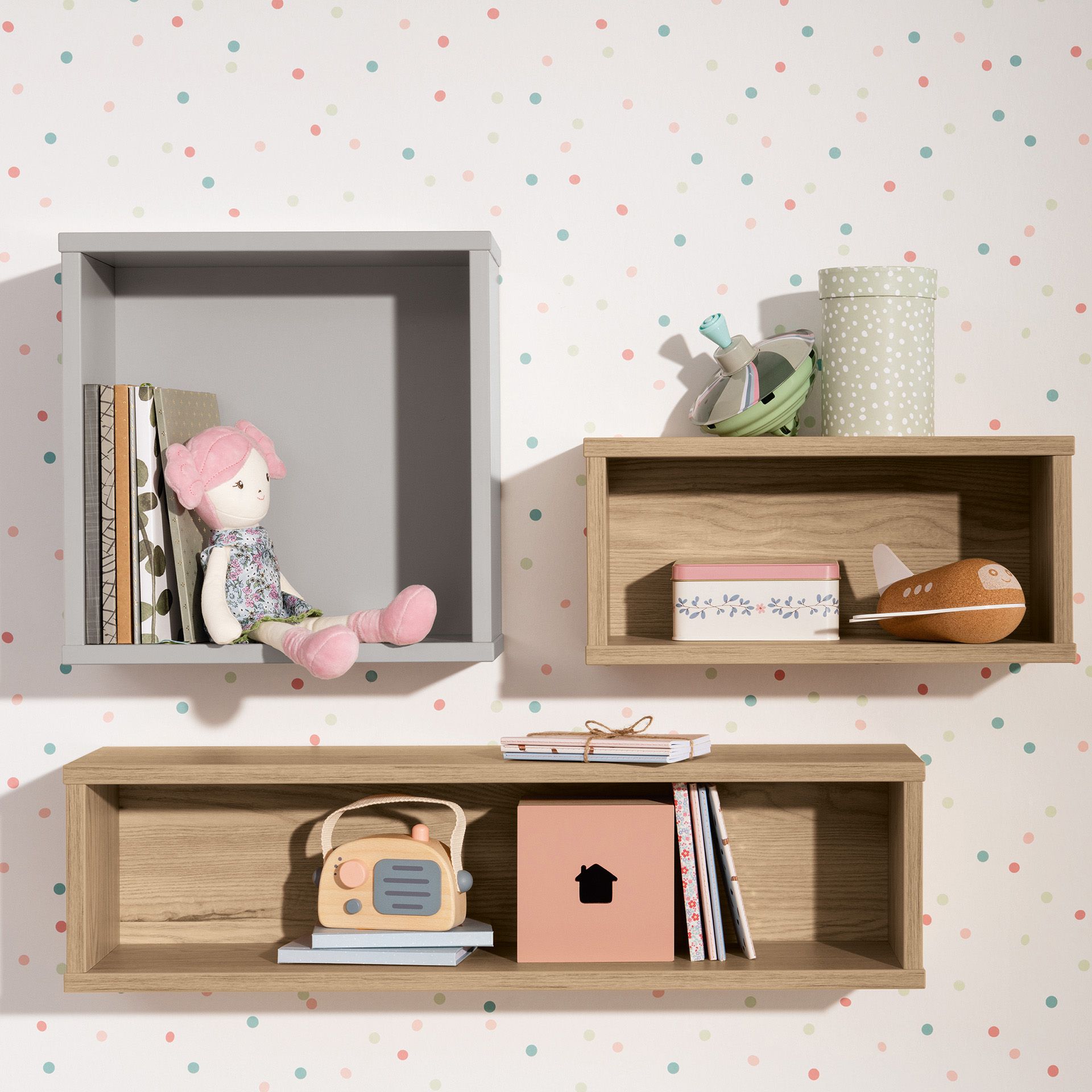 Wandregale mit Büchern, Spielzeug und Dekoration vor einer pastellfarbenen Wand mit Tupfen.