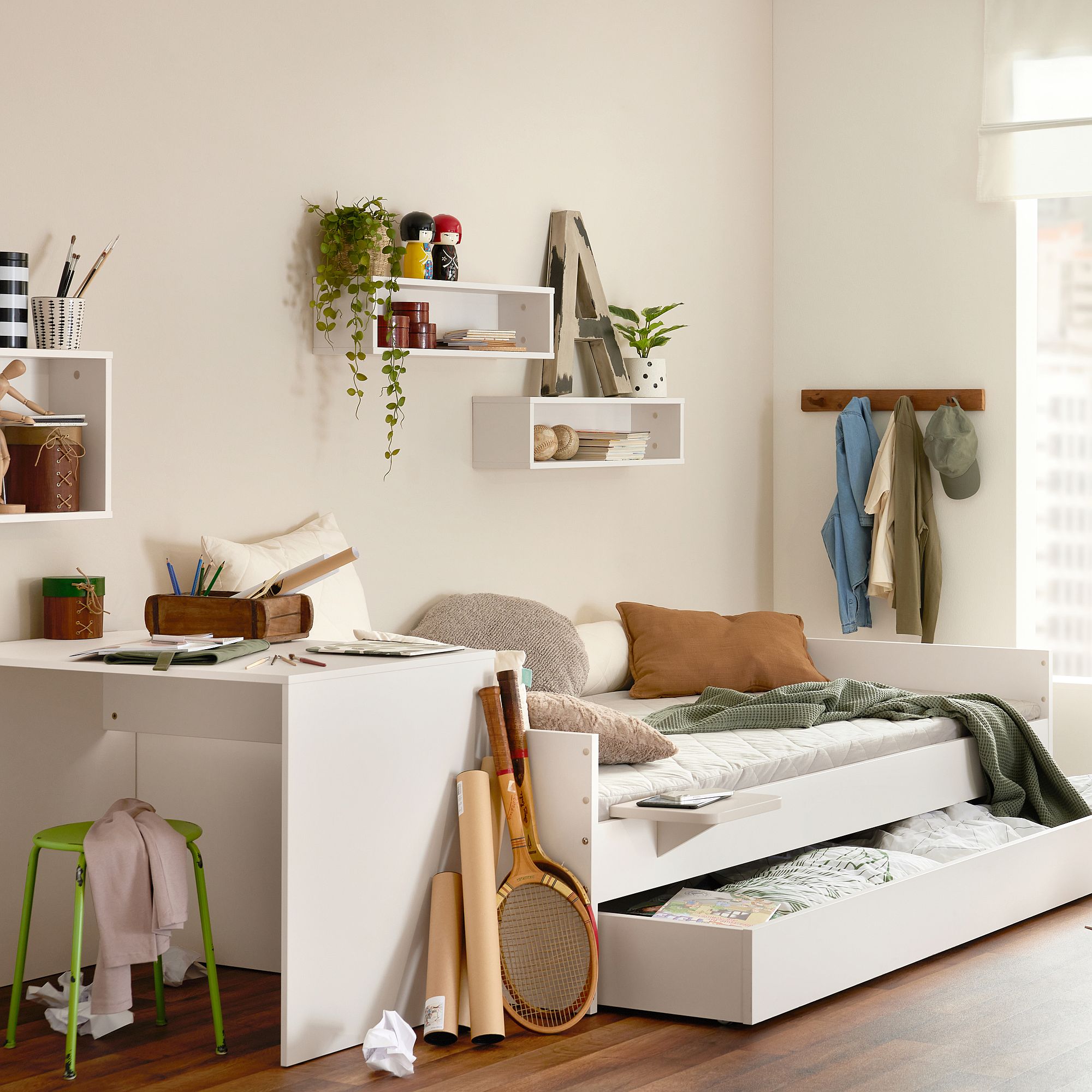 Gemütliches Schlafzimmer mit weißem Bett, ausziehbarer Schublade, Schreibtisch und Sportgeräten auf dem Boden.