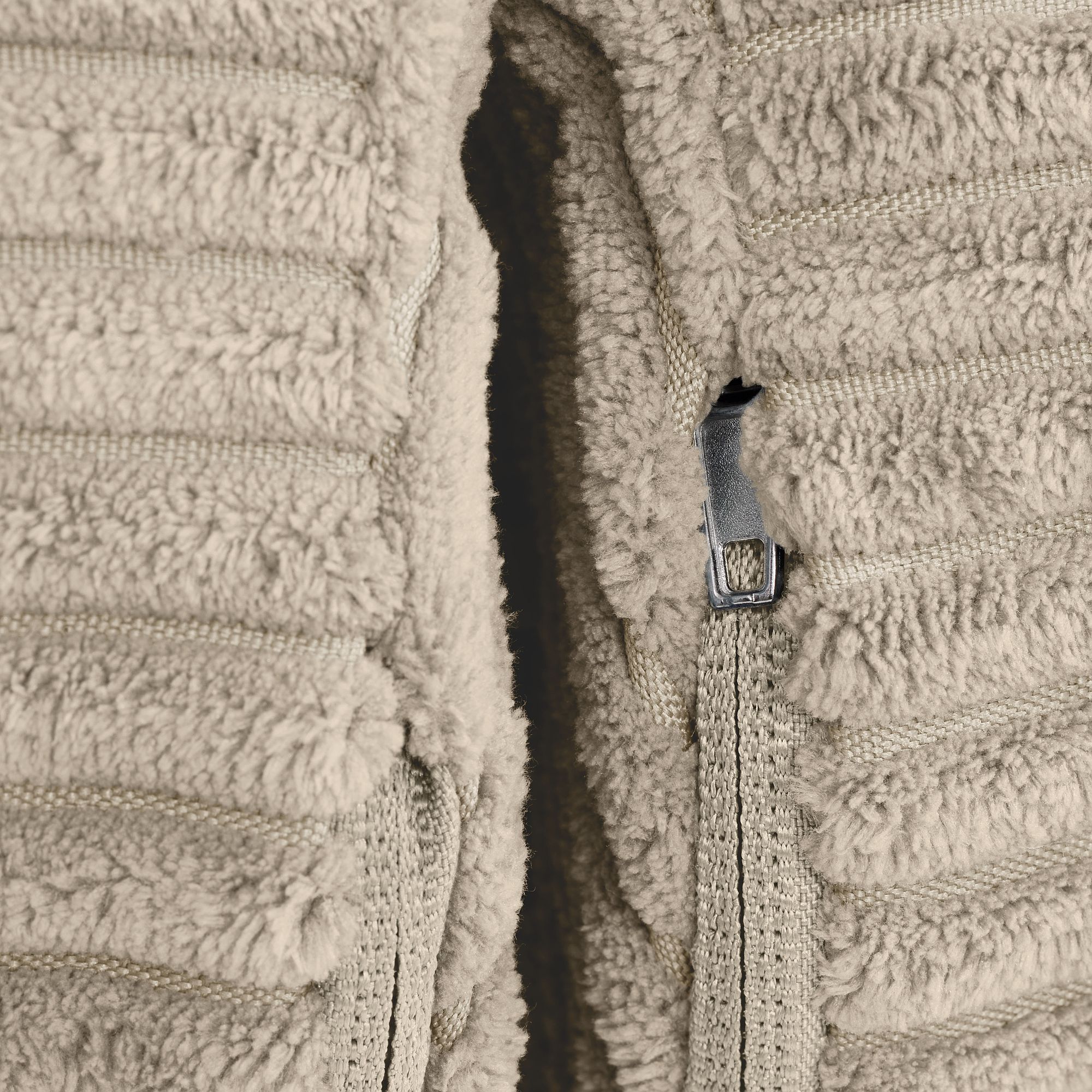 Nahaufnahme eines beigen, strukturierten Fleece-Kleidungsstücks mit einem teilweise geöffneten Reißverschluss.