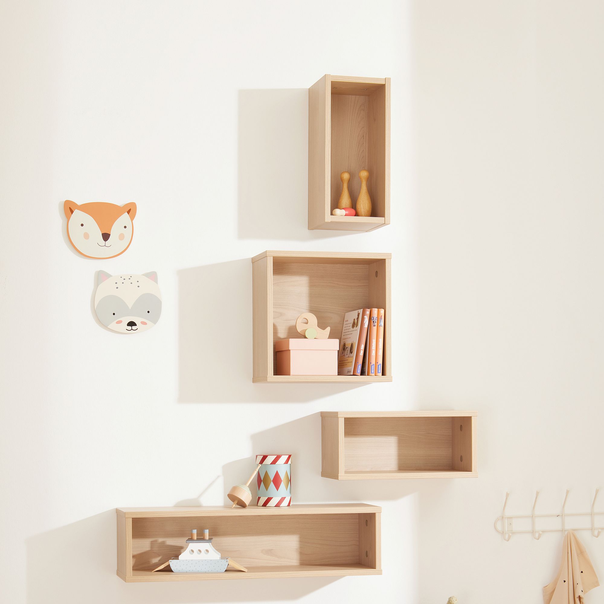 Hölzerne Wandregale mit Spielzeug, Büchern und Tiergesichtern an einer weißen Wand.