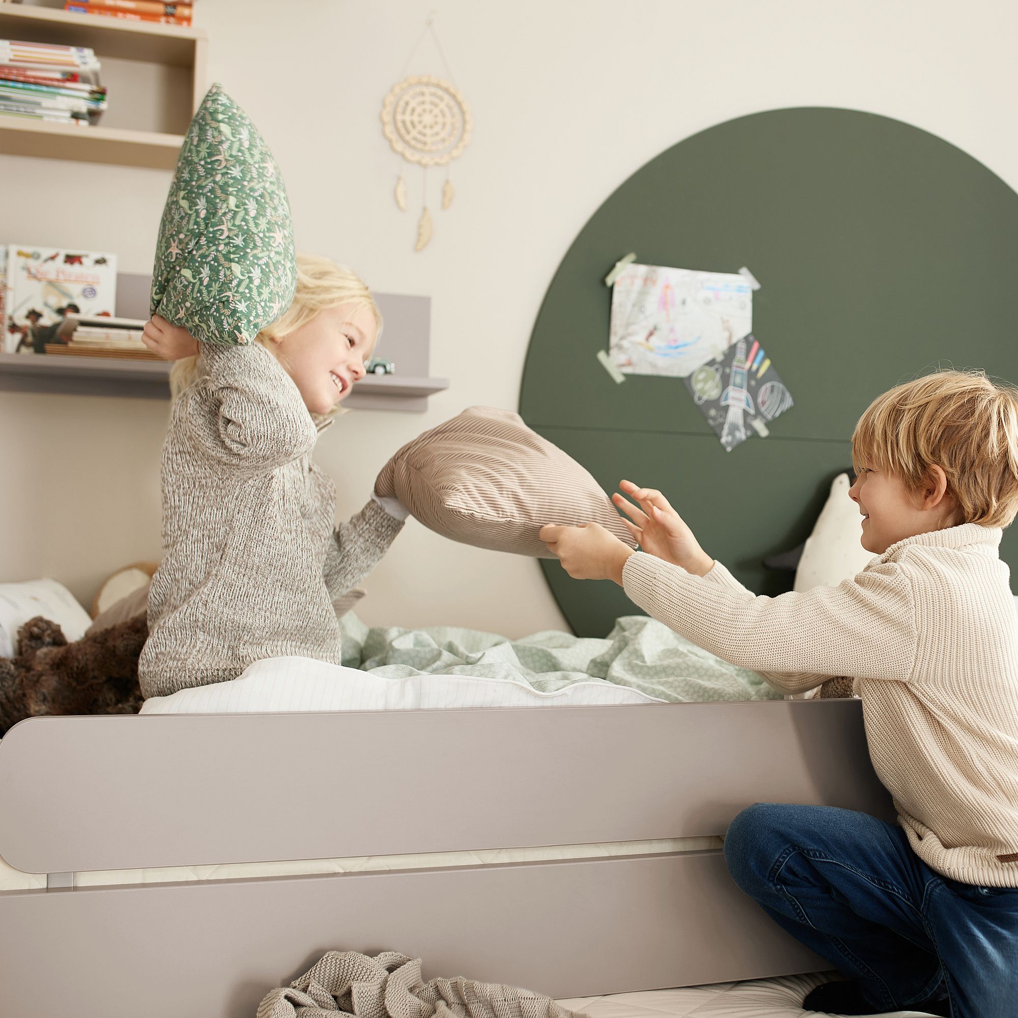 Zwei Kinder liefern sich eine Kissenschlacht auf einem Bett in einem gemütlich eingerichteten Zimmer.