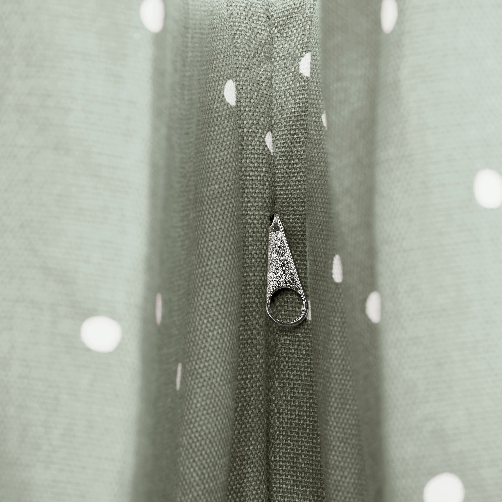 Nahaufnahme eines Reißverschlusses auf hellgrünem, weiß getupftem Stoff.