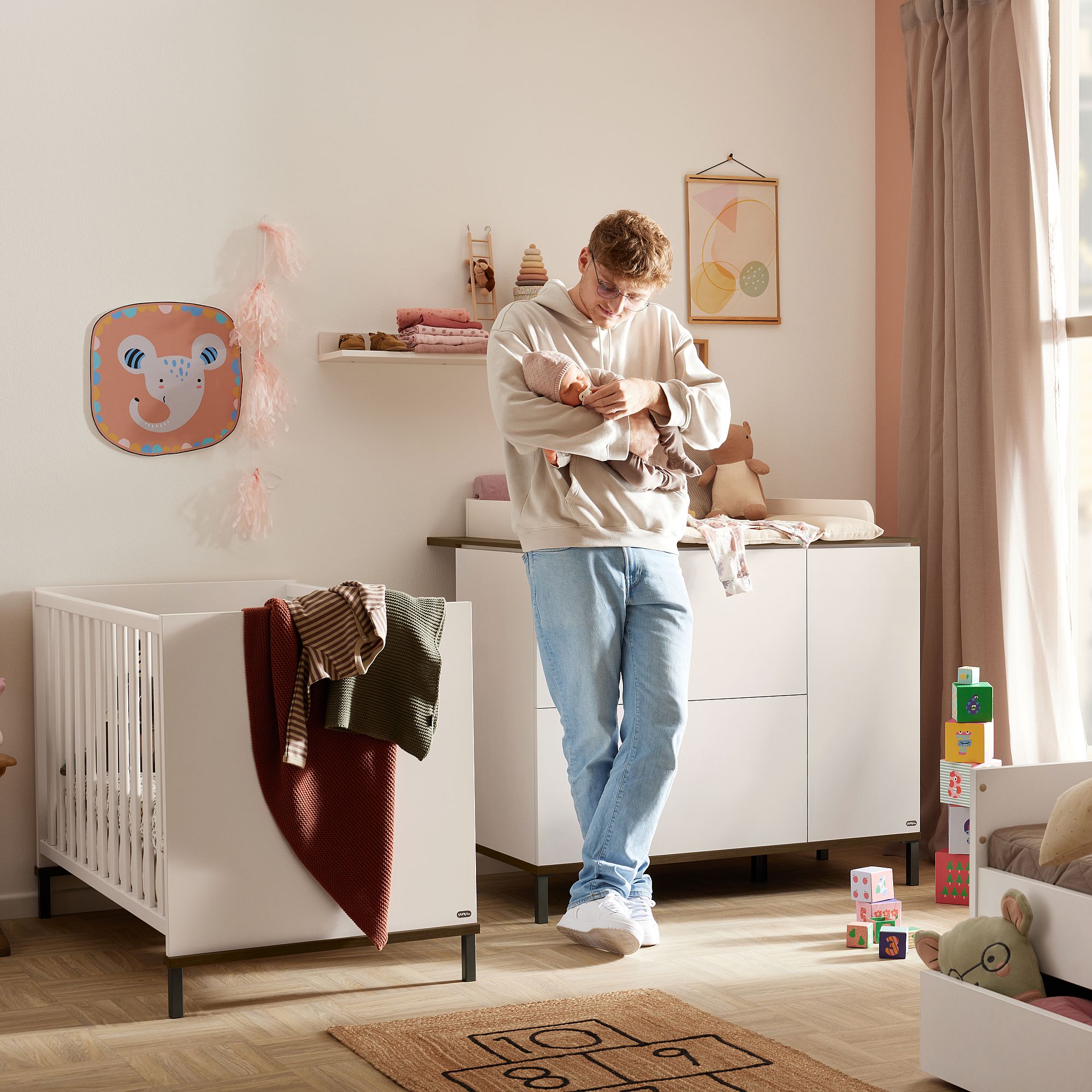Ein Mann wiegt ein Baby in einem gemütlichen, modernen Kinderzimmer mit einem Kinderbett und Spielzeug.