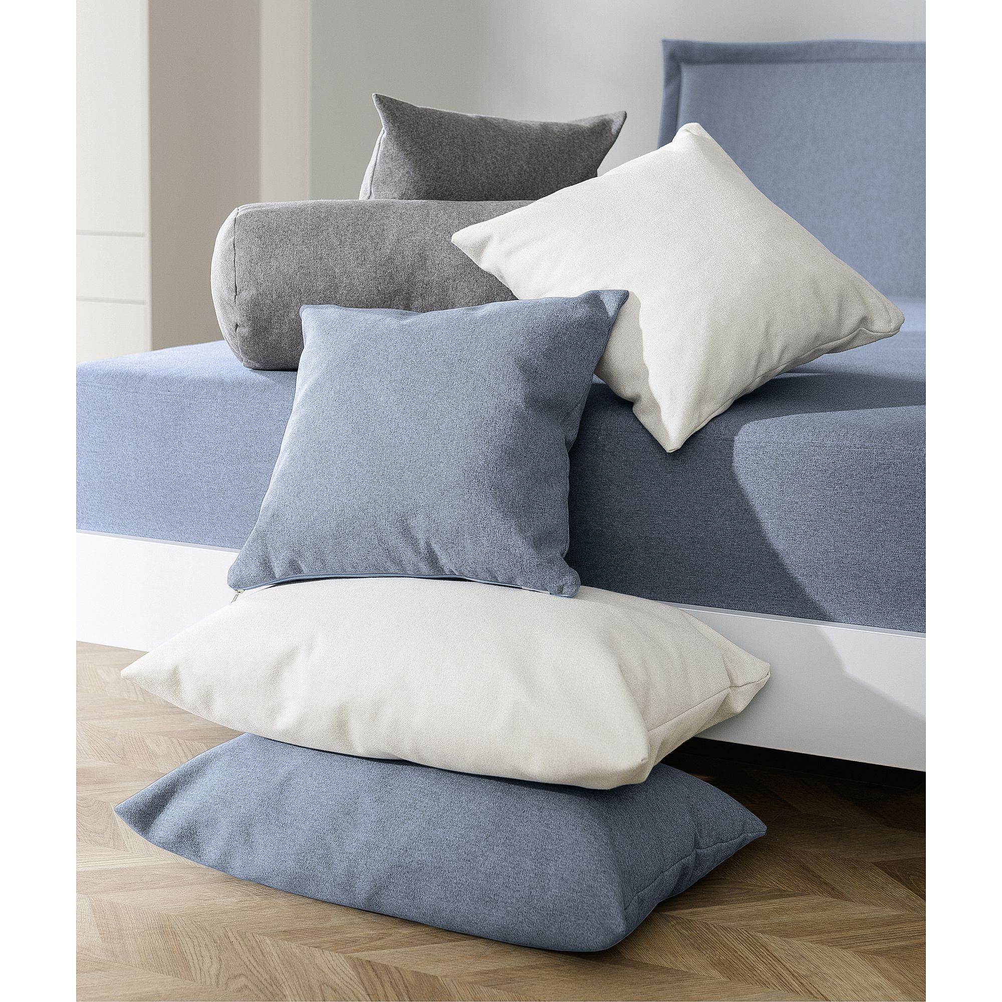 Gestapelte blaue und weiße Kissen auf einem Bett mit passender blauer und grauer Bettwäsche.