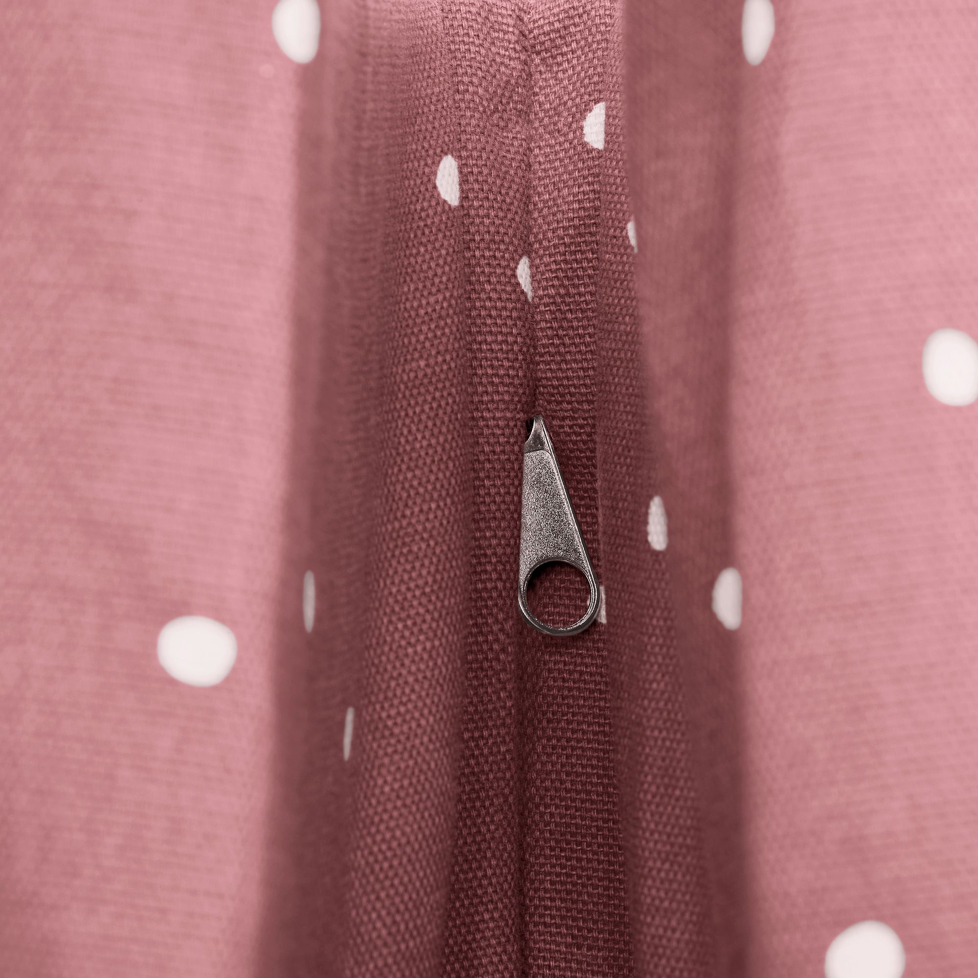Nahaufnahme eines Reißverschlusses auf rosa Stoff mit weißen Tupfen.