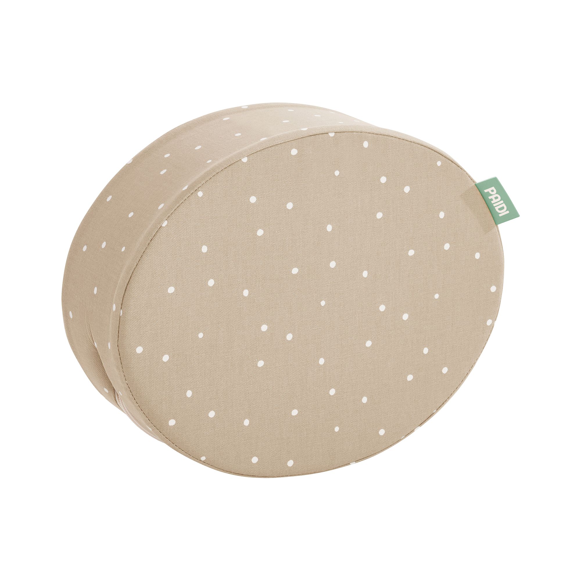 Beigefarbenes rundes Kissen mit weißen Tupfen und einem kleinen grünen Stoffanhänger.