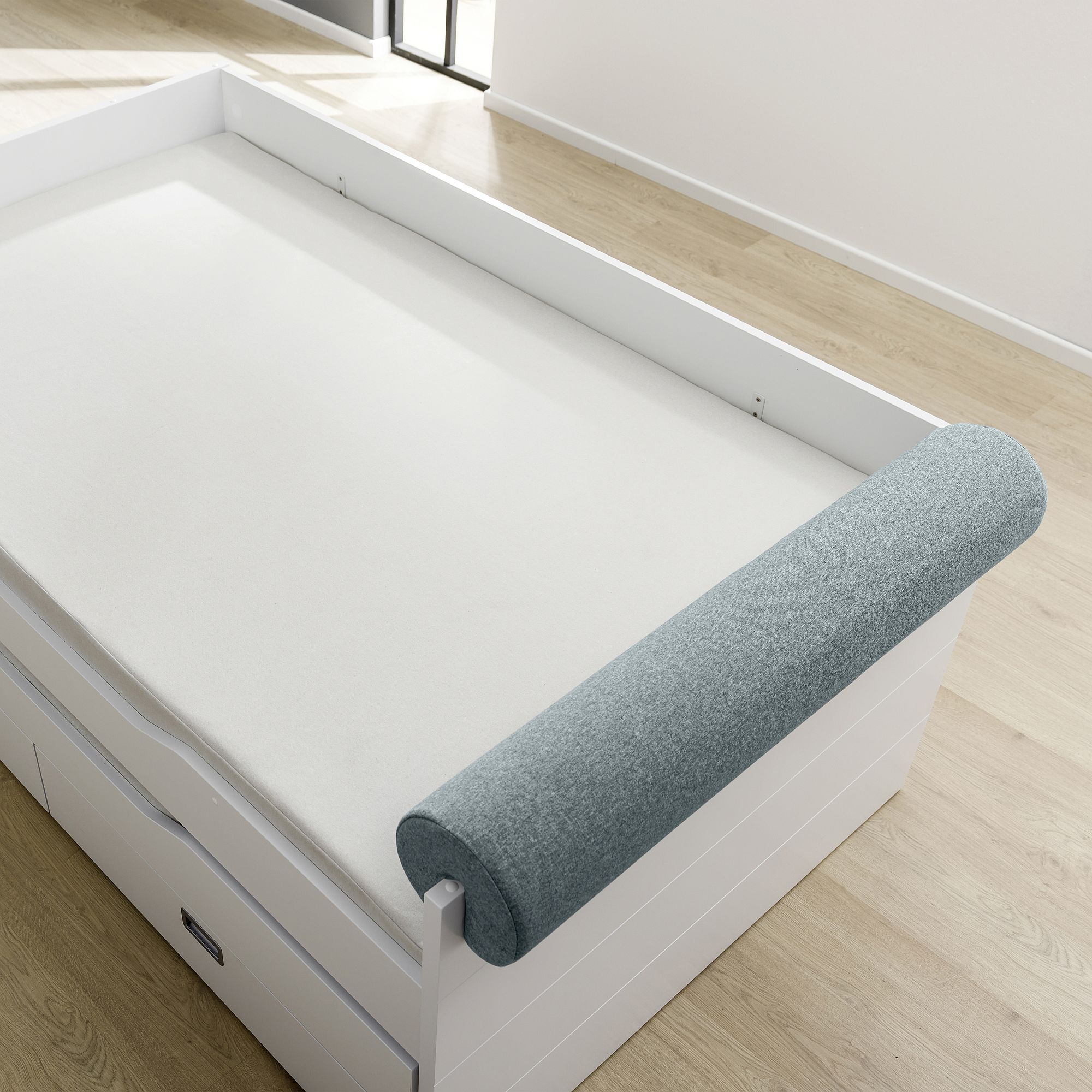 Ein weißes Bett mit einem grauen zylindrischen Kissen an einem Ende auf einem Holzboden.