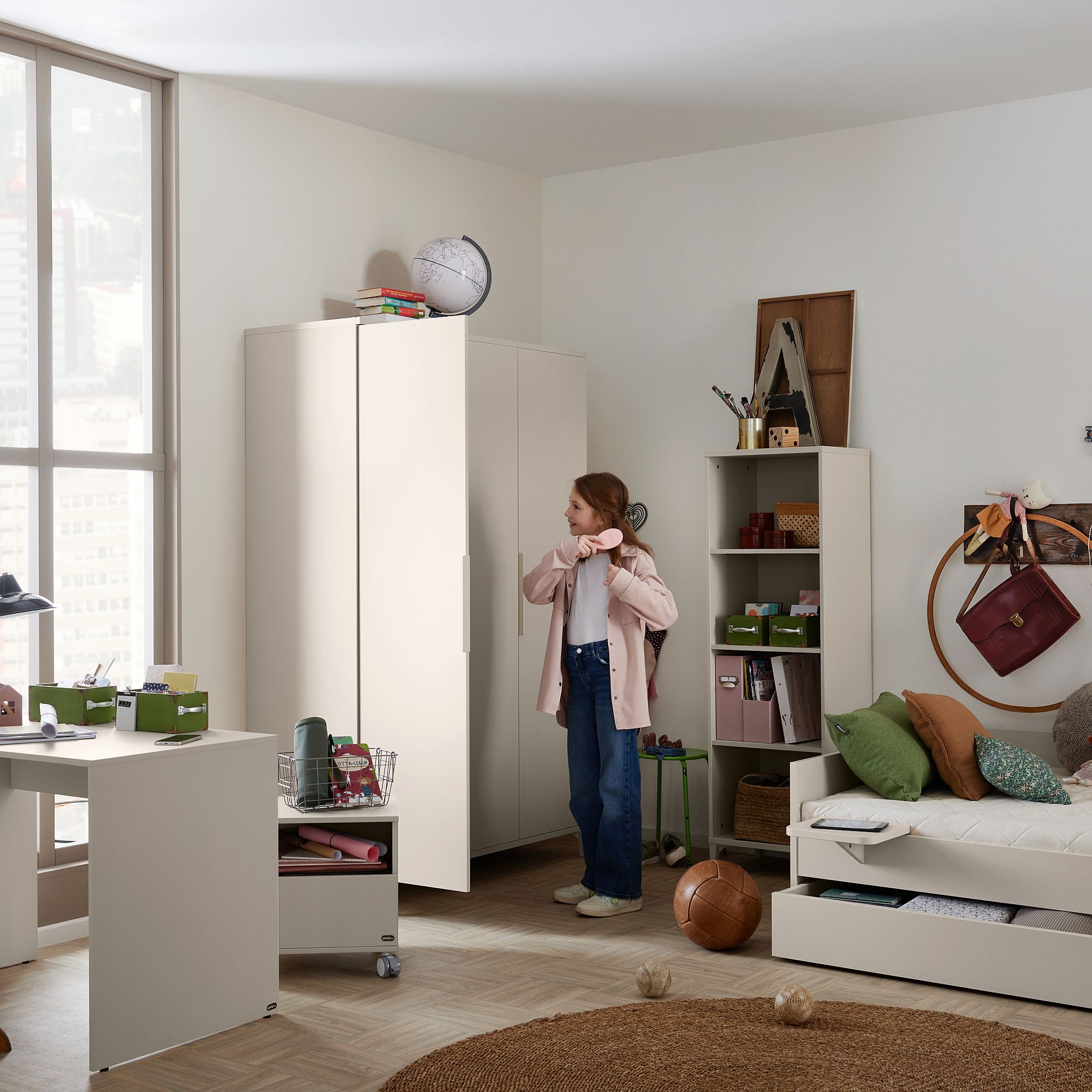 Ein Mädchen steht in einem aufgeräumten, modernen Schlafzimmer mit Regalen, Schreibtisch und Kleiderschrank.