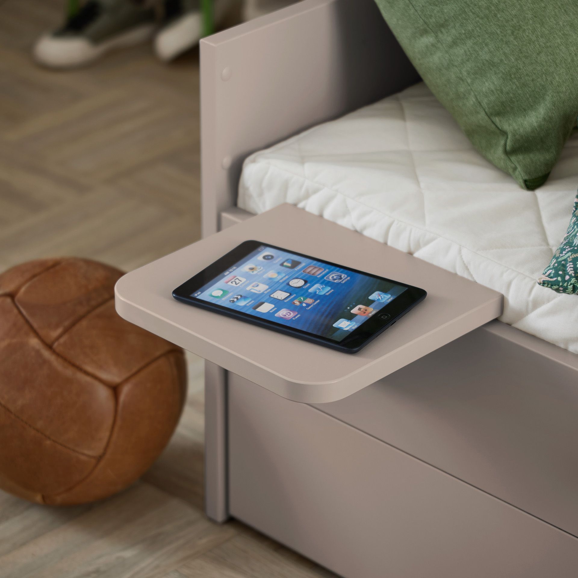 Ein Tablet liegt auf einem kleinen Nachttisch neben einem Bett mit grünen Kissen.