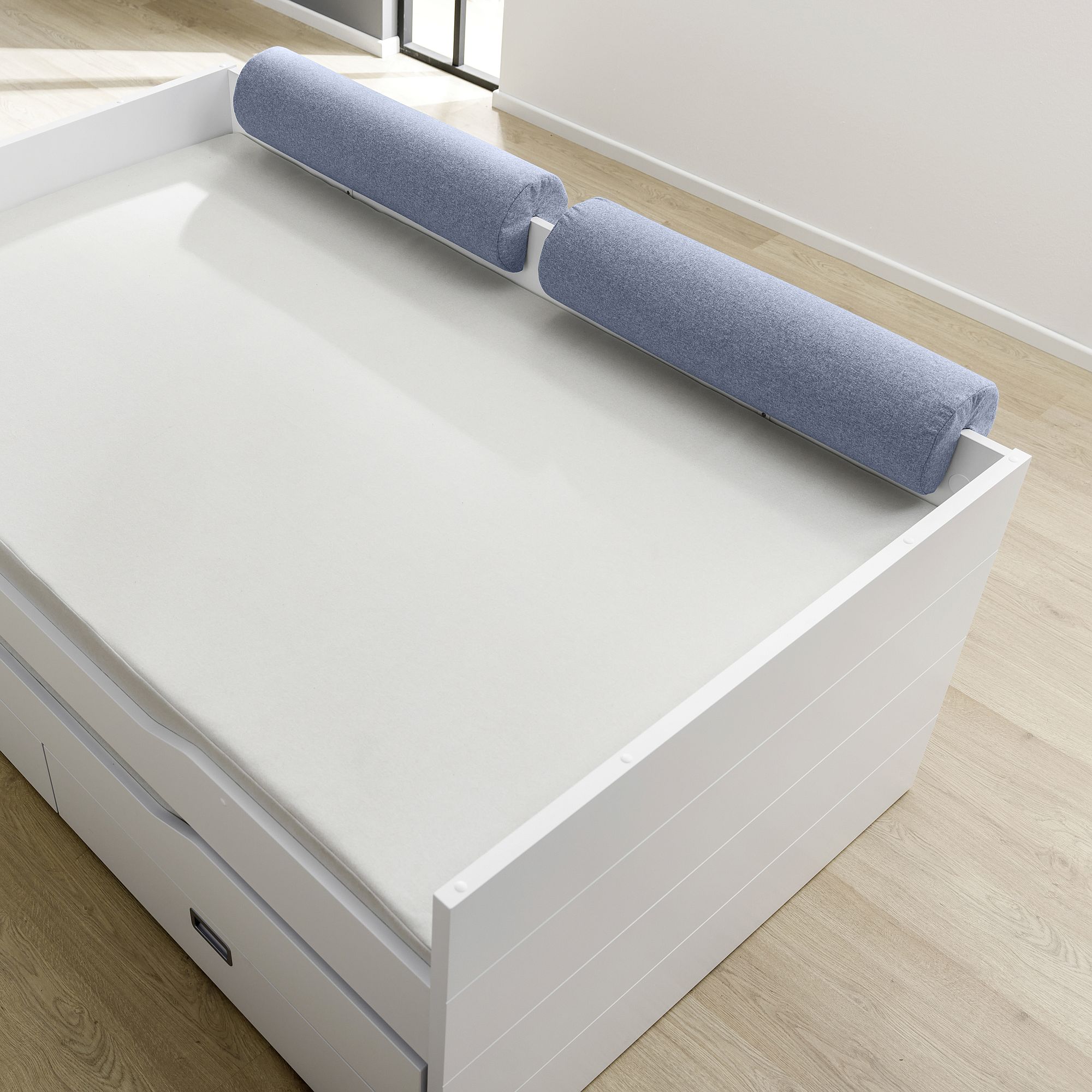 Comfort-Rolle 85,30 x Ø 20 cm, Mikrofaser Tintenblau Weißes Bett mit zwei zylindrischen blauen Kissen auf dem Kopfteil in einem hellen Raum.