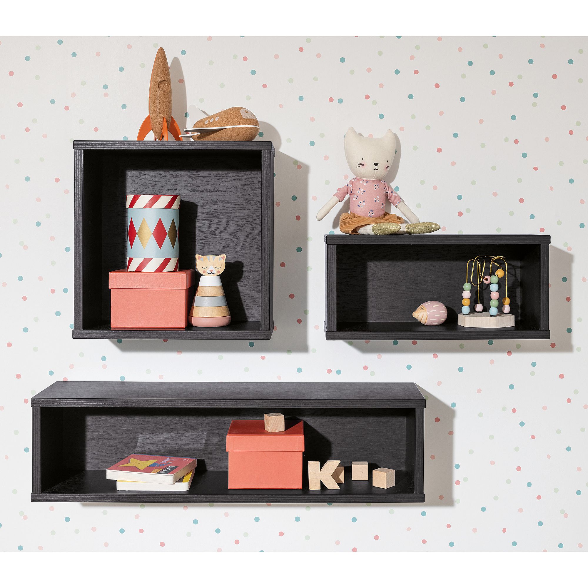 Drei schwarze Wandregale mit Spielzeug, Büchern und Kisten vor einer gepunkteten Wand.