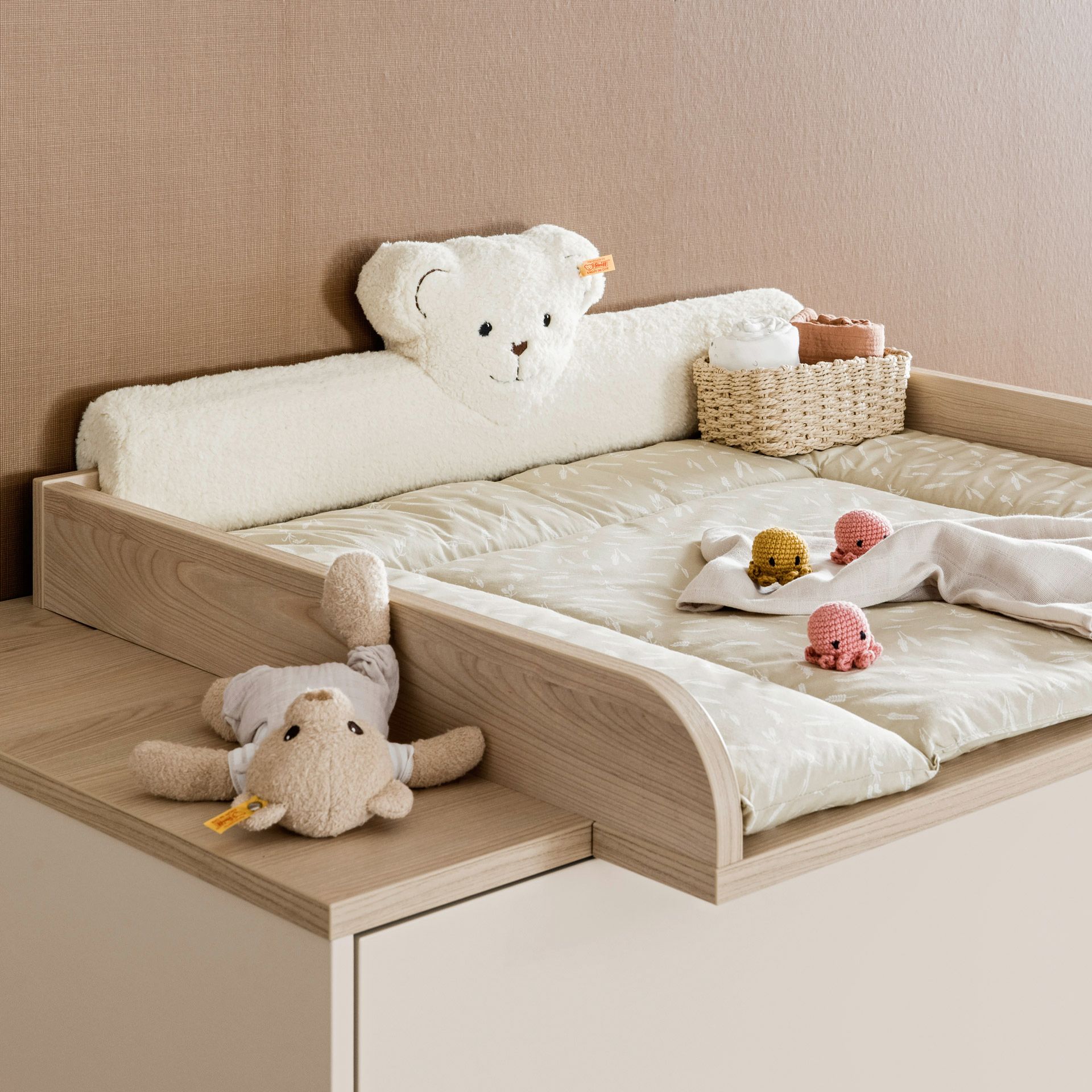 Kopfschutz Steiff by PAIDI Kissen für Wickelaufsatz, Beige Wickeltisch mit Bärenkissen, Korb und Plüschtieren oben drauf.