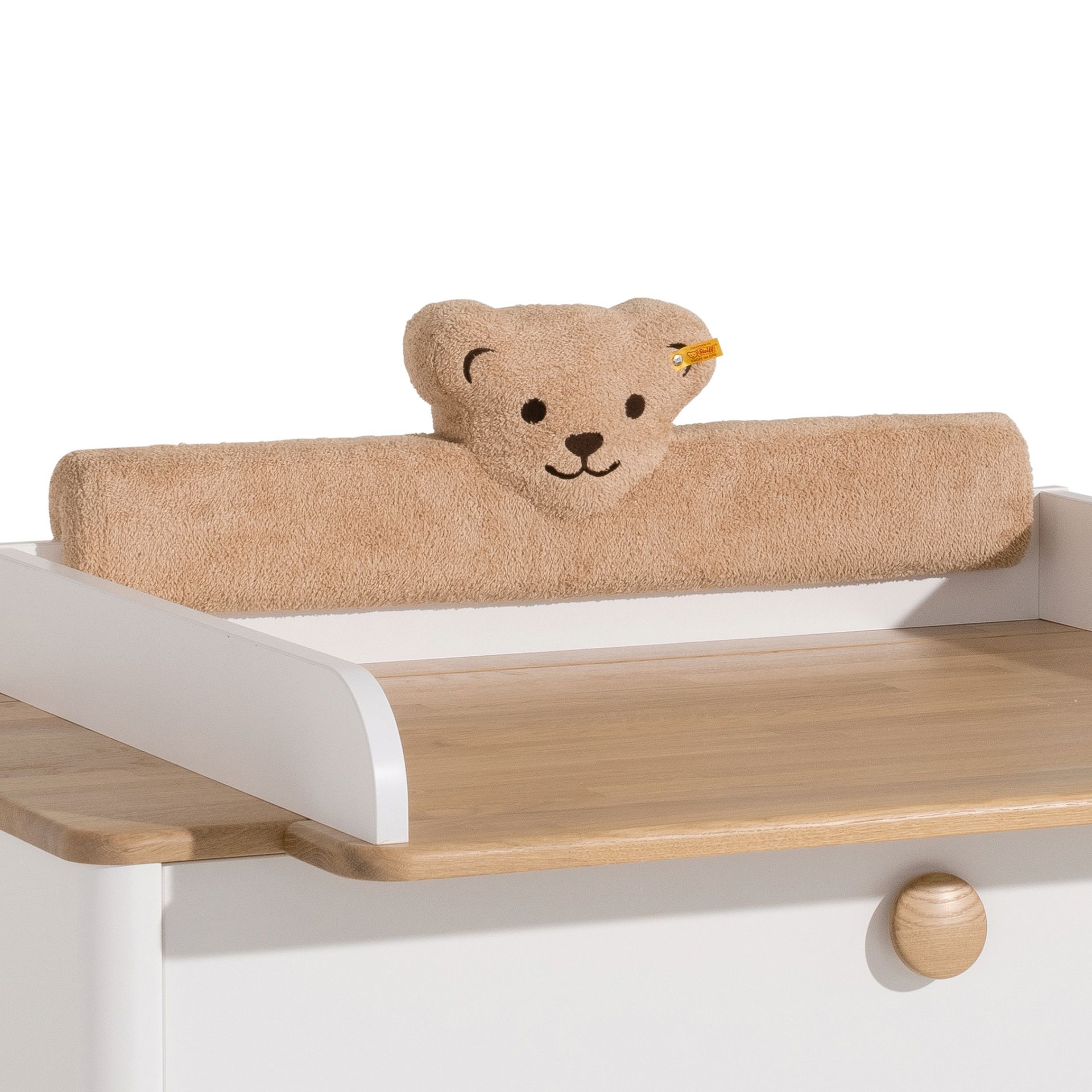 Kopfschutz Steiff by PAIDI Kissen für Wickelaufsatz, Braun Ein zusammengerolltes Handtuch mit einem Teddybärgesicht auf einem hölzernen Wickeltisch.