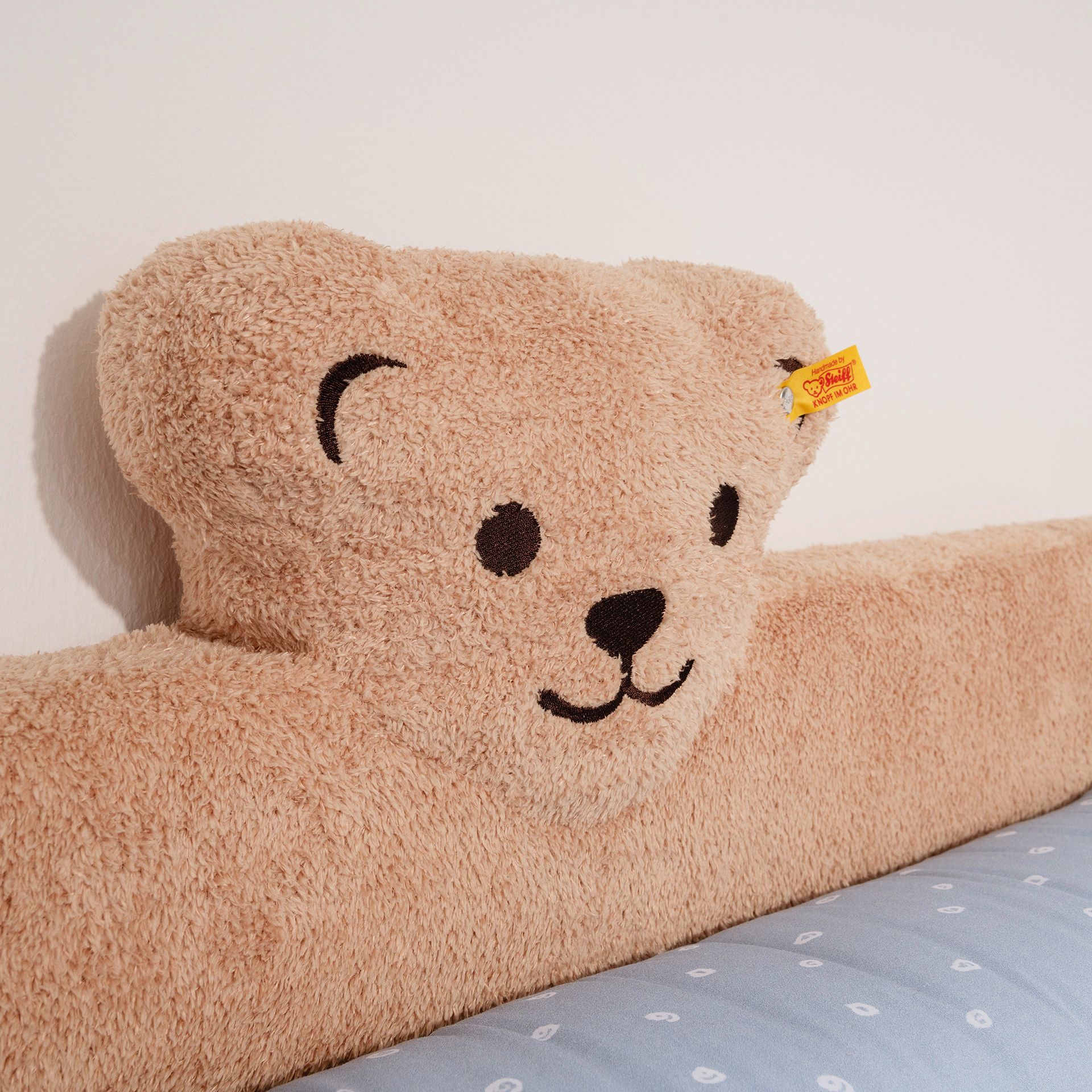 Plüschkissen in Form eines Teddybären, das an einer weißen Wand über einem blauen Bett ruht.
