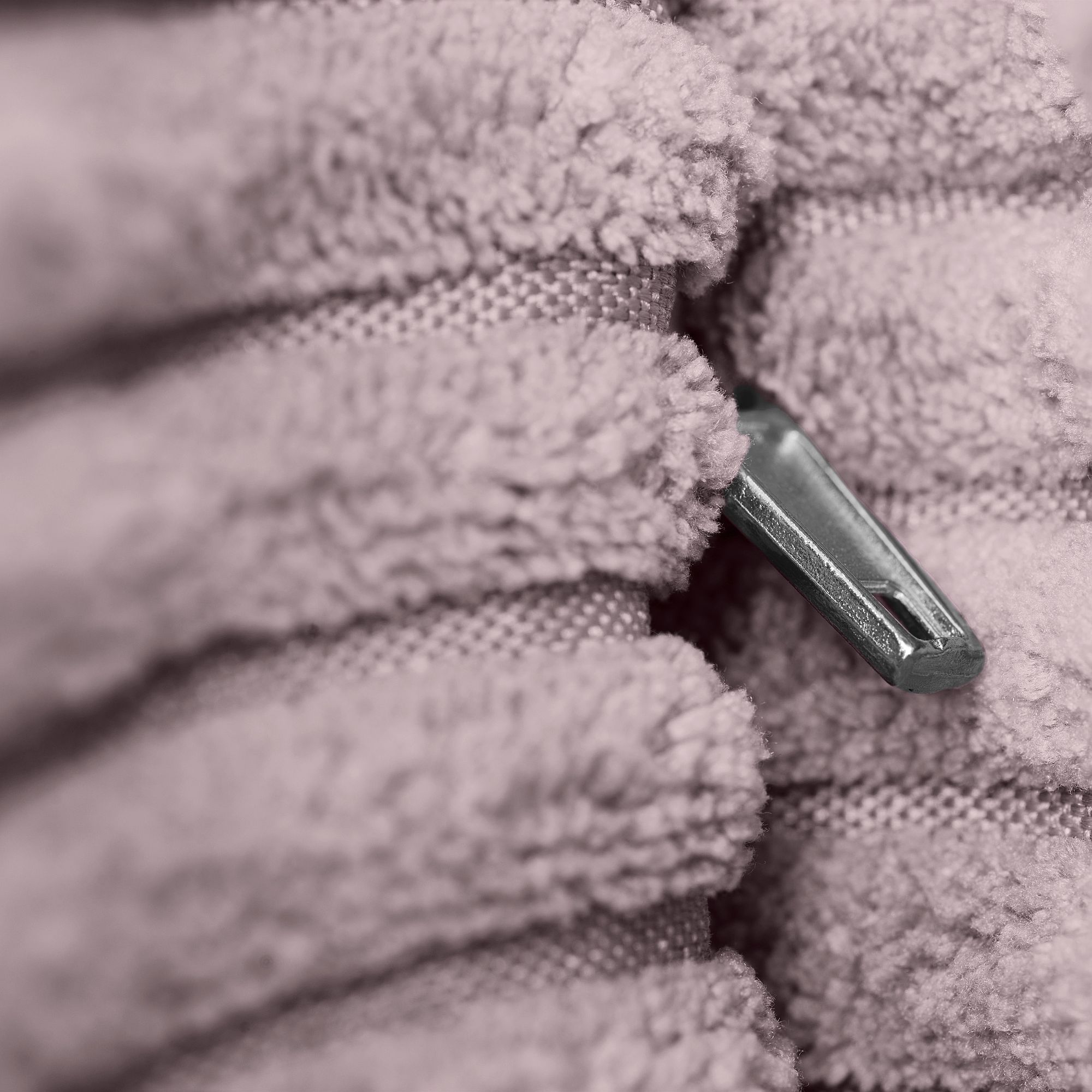 Eine Nahaufnahme eines silbernen Reißverschlusses, der teilweise in einem dicken, strukturierten rosa Stoff verborgen ist.