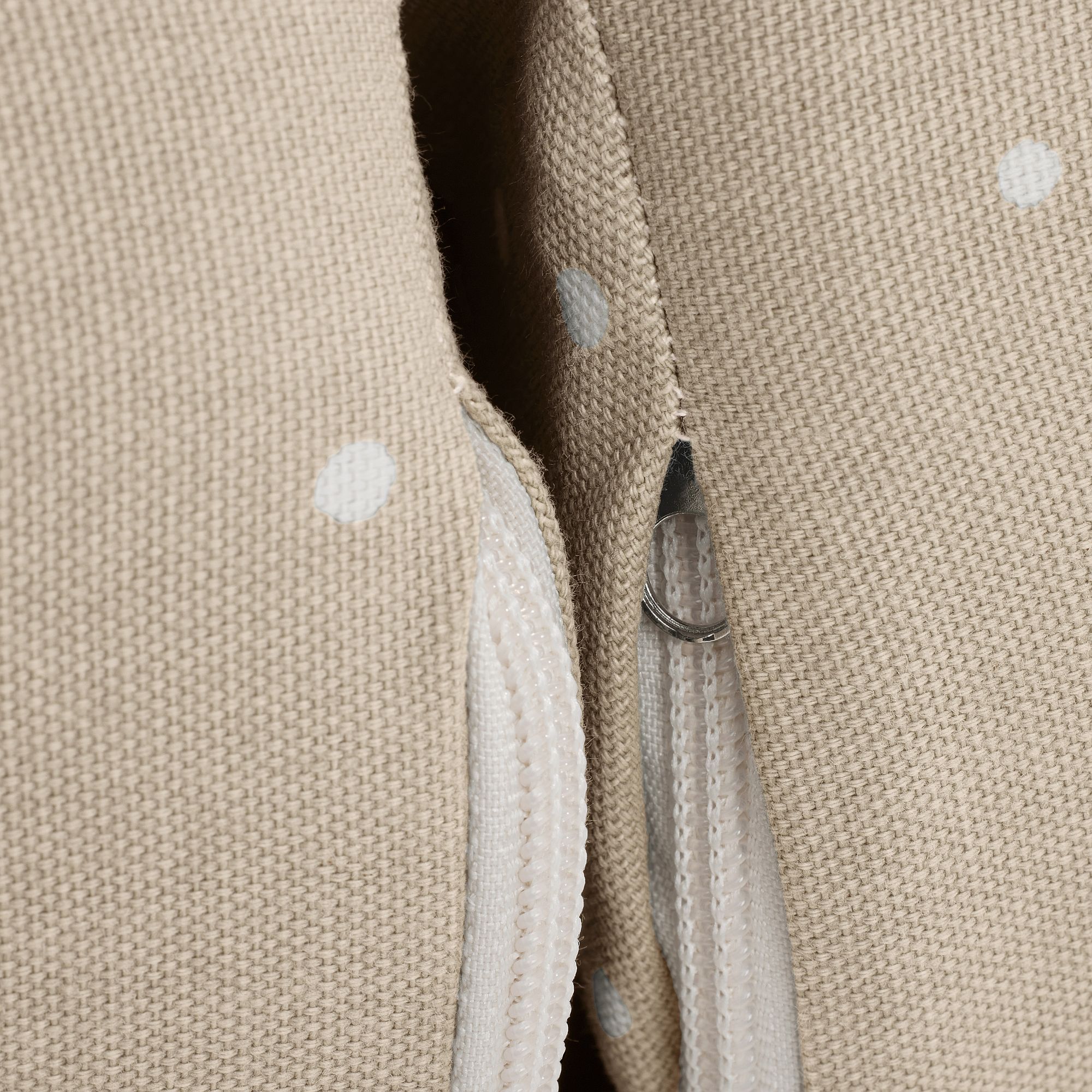 Nahaufnahme von beigem Stoff mit weißen Punkten und einem teilweise sichtbaren Reißverschluss.