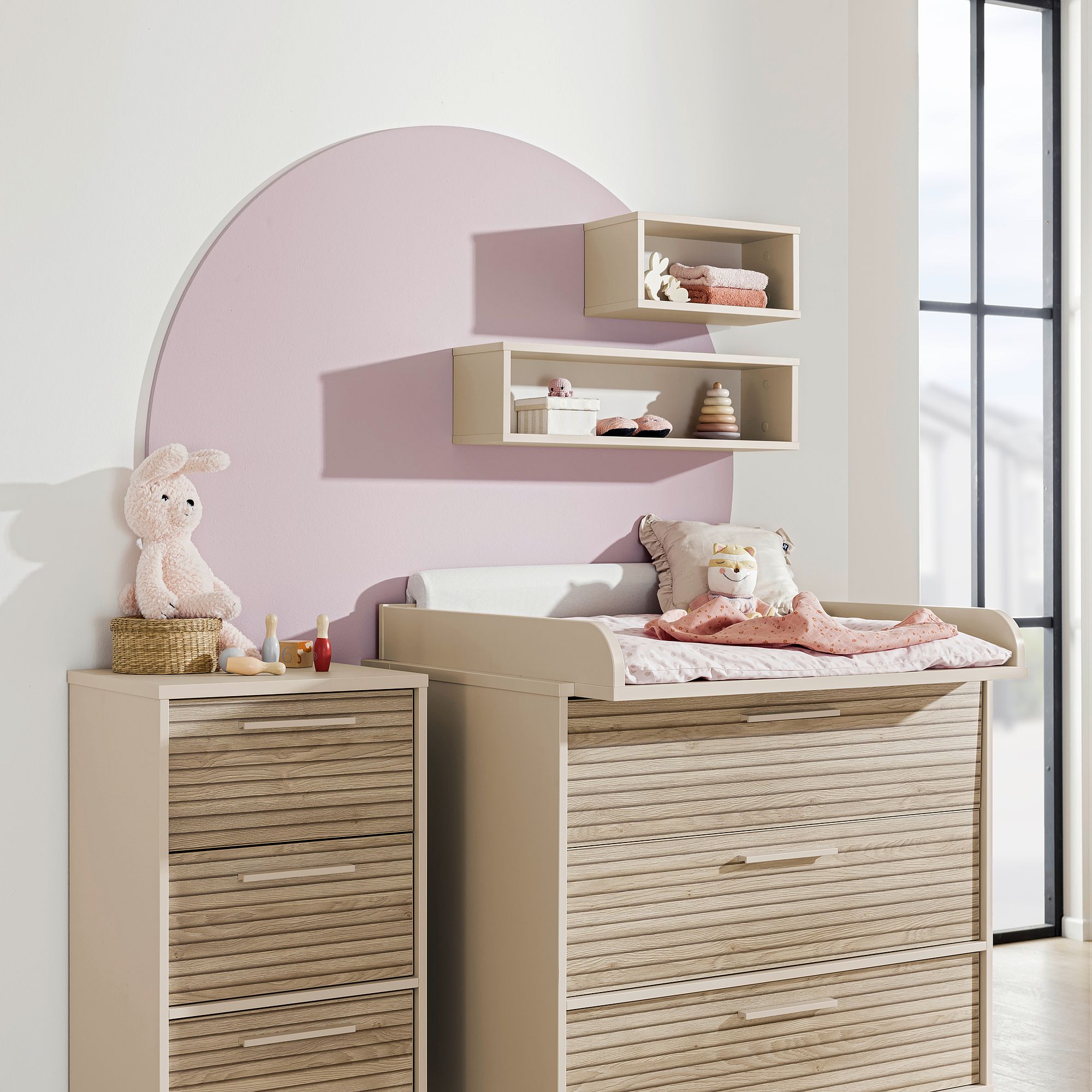 Modernes Kinderzimmer mit einer rosa Akzentwand, Kommode, Wickeltisch und Plüschhase.