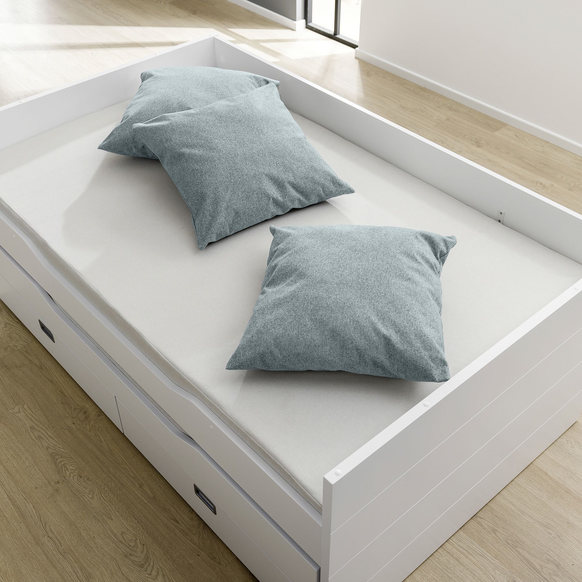 Ein weißes Bett mit zwei grauen Kissen auf einem hellen Holzboden.
