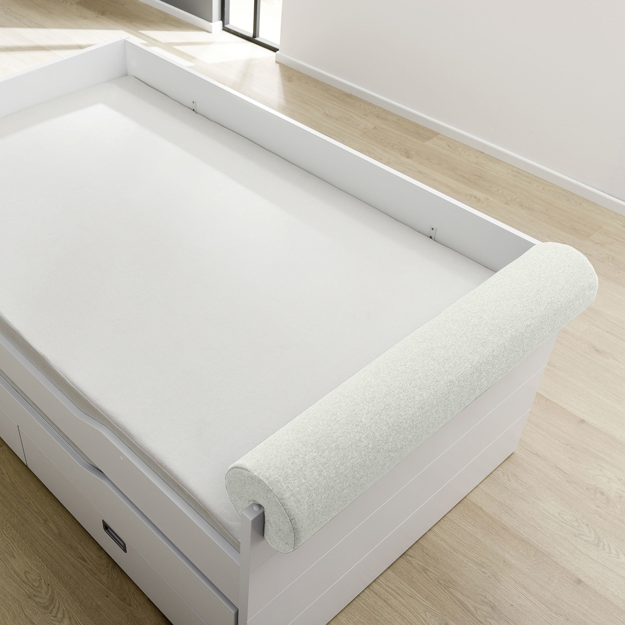 Comfort-Rolle 115 x Ø 20 cm, Mikrofaser Ivory Eine weiße aufrollbare Matratzenauflage auf einem weißen Bettgestell mit Schubladen.