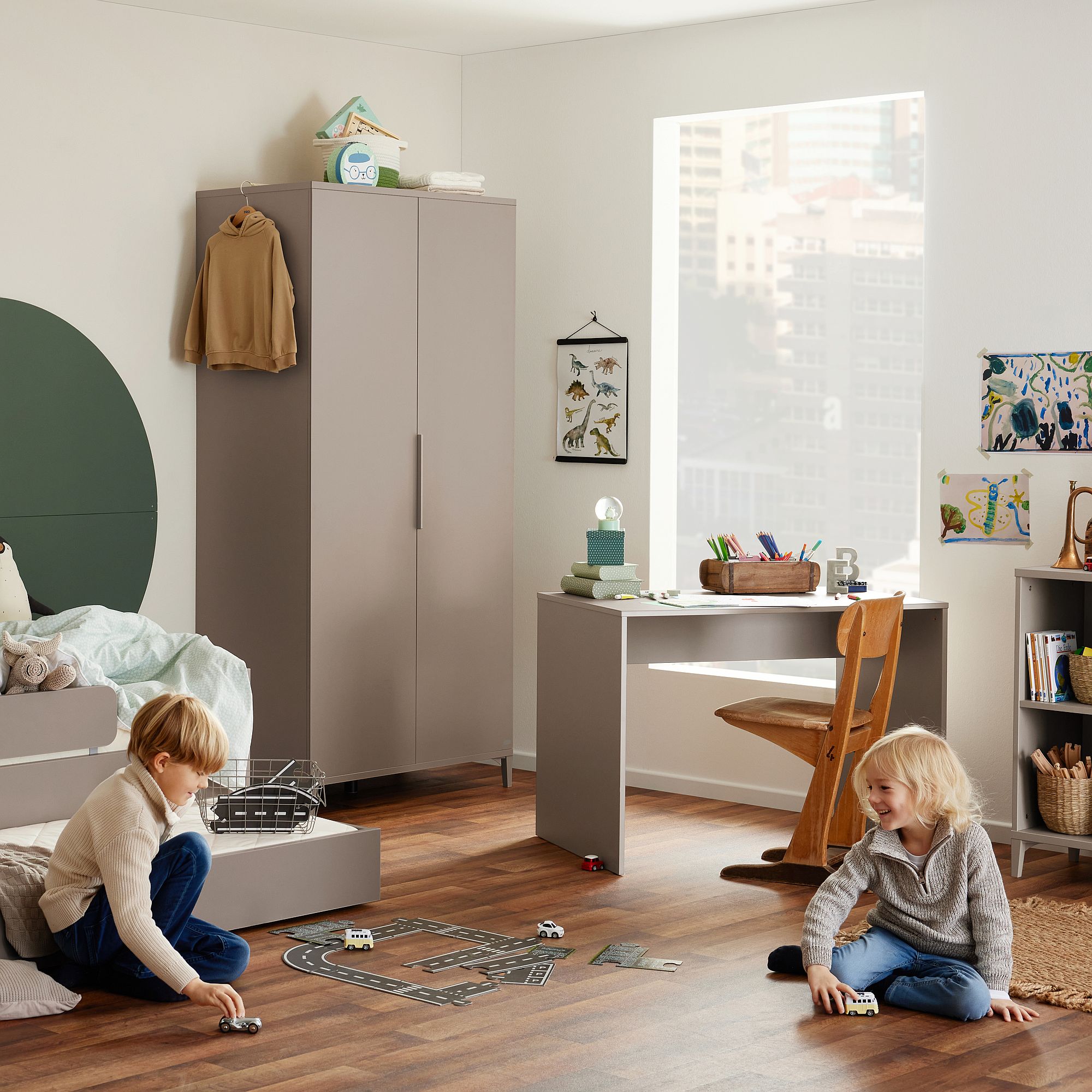 Zwei Kinder spielen mit Spielzeugautos auf dem Boden in einem hellen, modernen Schlafzimmer.