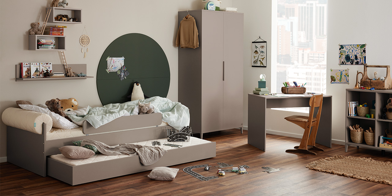 Kinderzimmer mit zwei Betten, Schreibtisch, Regale, Spielzeug, Bücher und Blick auf die Stadt durch das Fenster. Das Zimmer ist aufgeräumt und gut organisiert.