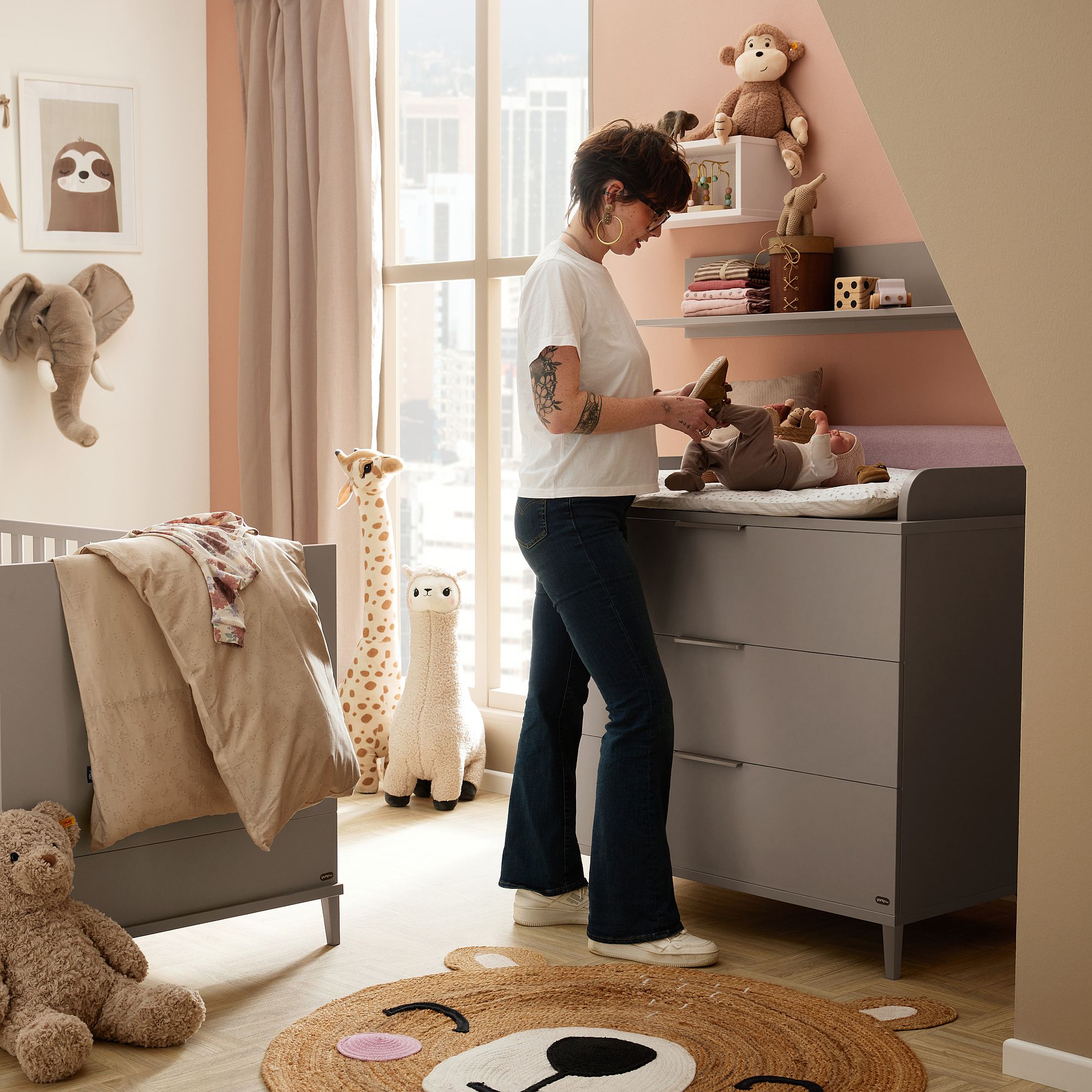 Eine Frau wickelt ein Baby in einem mit Plüschtieren und Spielzeug dekorierten Kinderzimmer.