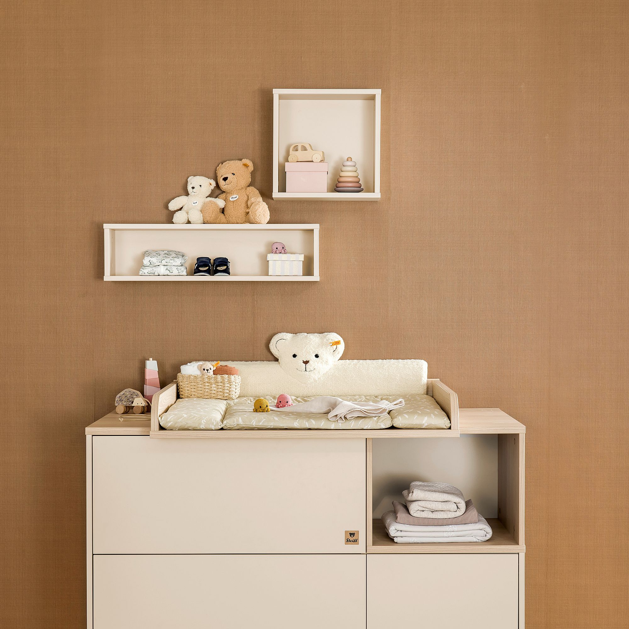 Neutrales Kinderzimmer mit Spielzeug, einem Wickeltisch und Babyzubehör vor einer braunen Wand.