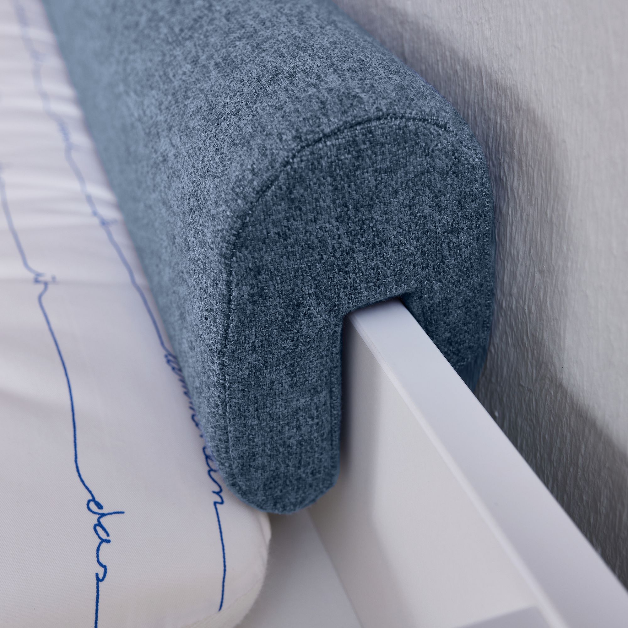 Blauer Bettschutz aus Stoff, der an der Seite eines weißen Bettrahmens befestigt ist.