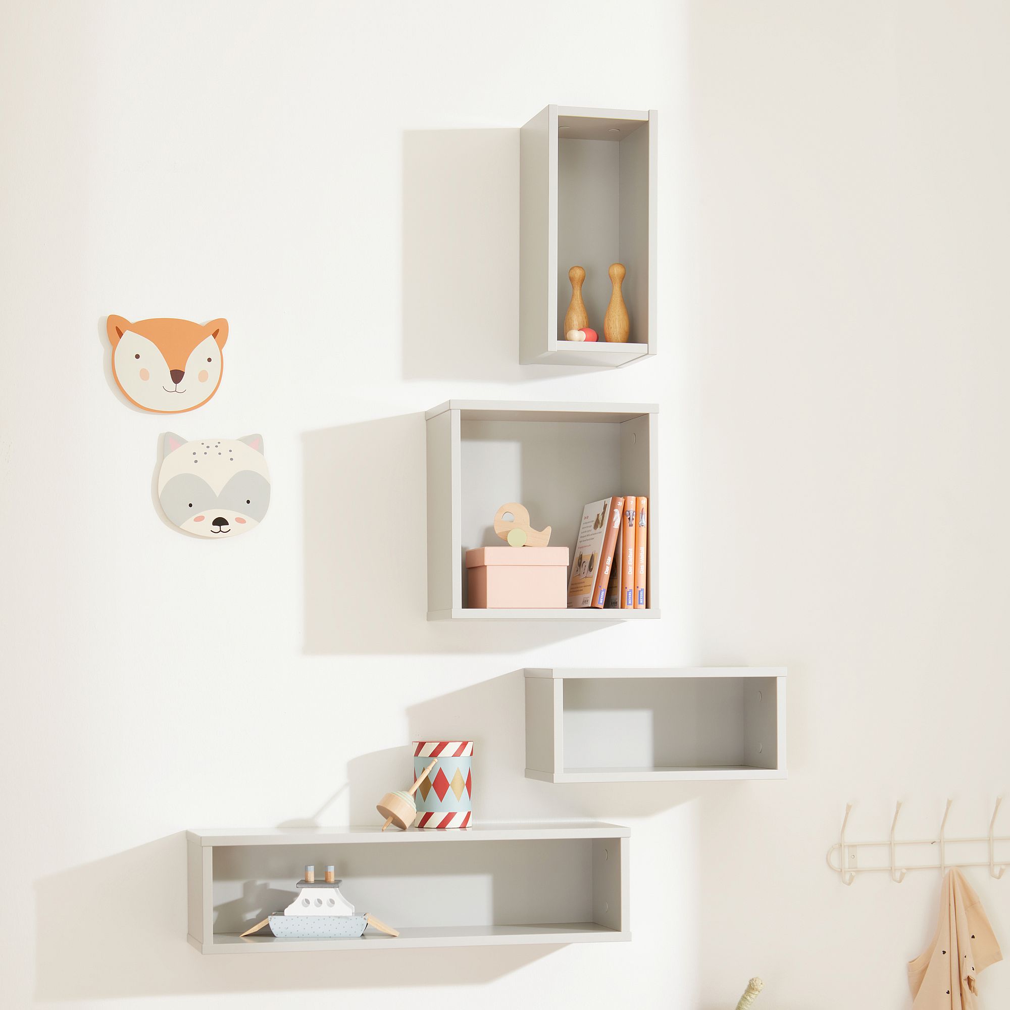 Vier graue Wandregale mit Spielzeug, Büchern und Wanddekoration mit Tiergesichtern darüber.