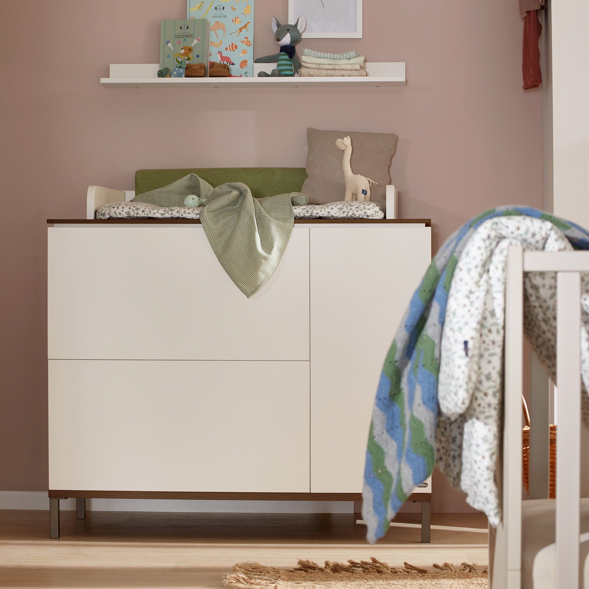 Moderner Wickeltisch mit Spielzeug und einer Decke in einem gemütlichen Kinderzimmer.