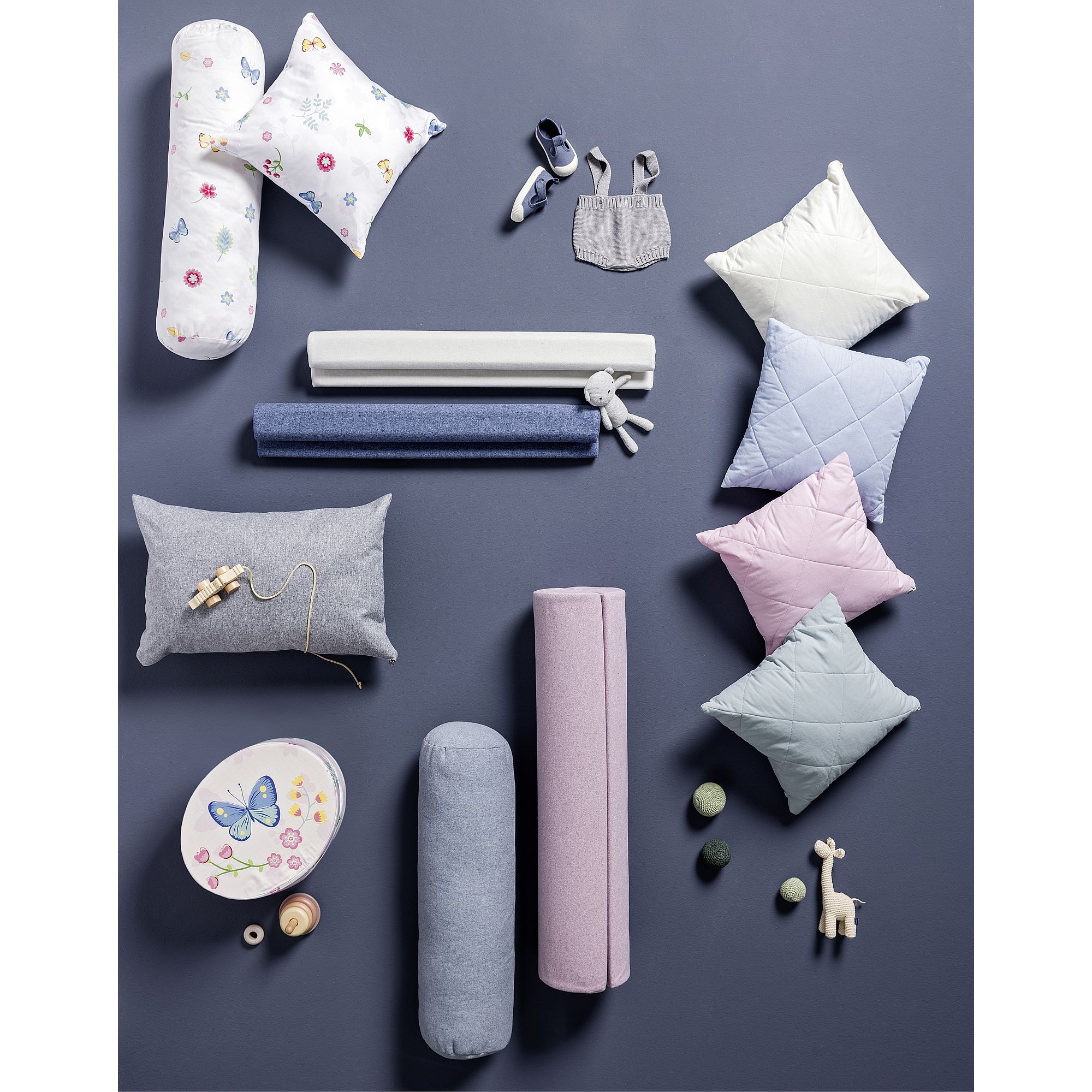 Baby-Kissen, Spielzeug, Kleidung und weiche Nackenrollen auf einem lila Hintergrund.