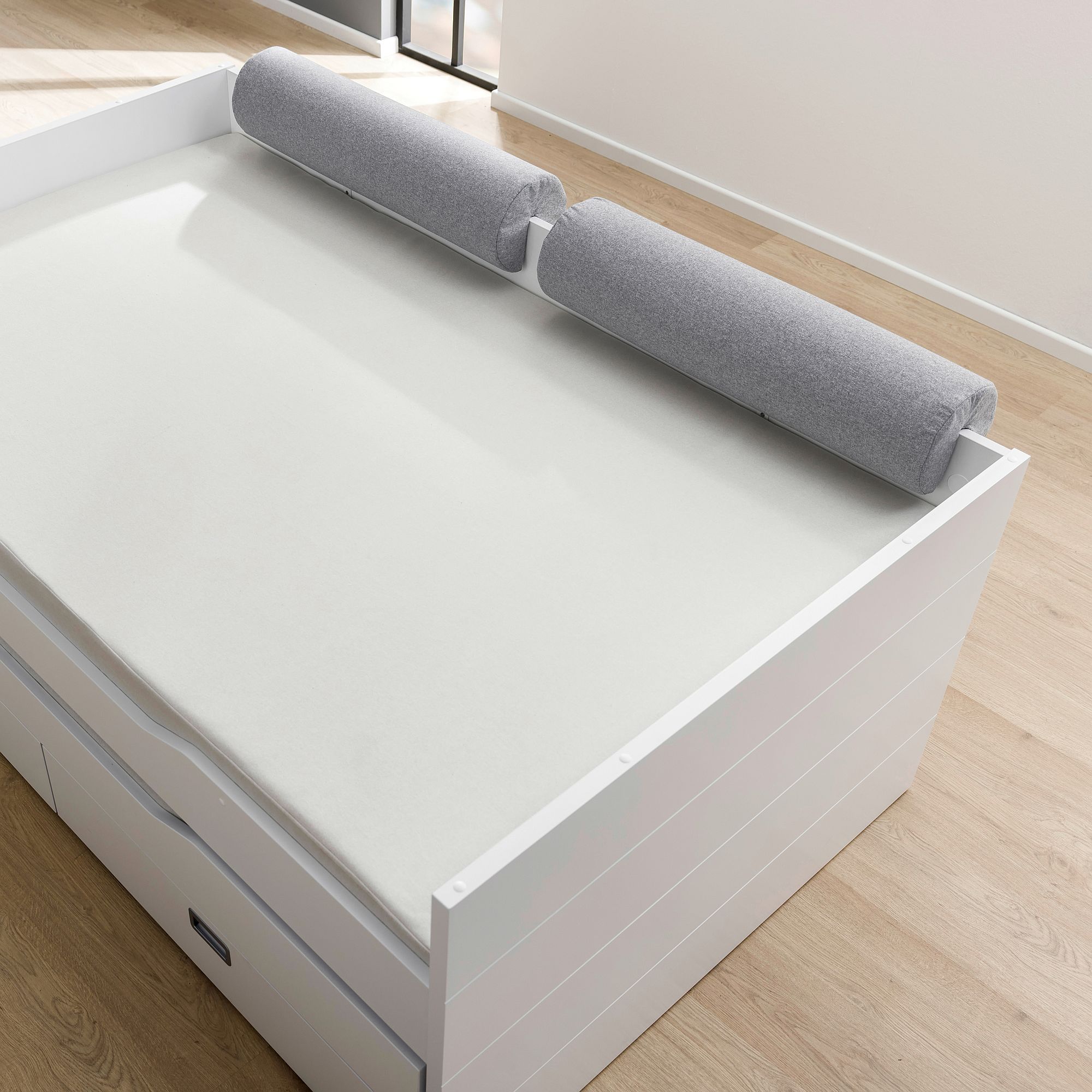Comfort-Rolle 85,30 x Ø 20 cm, Mikrofaser Steingrau Weißes Bett mit zwei grauen zylindrischen Kissen am Kopfende, auf einem hellen Holzboden.