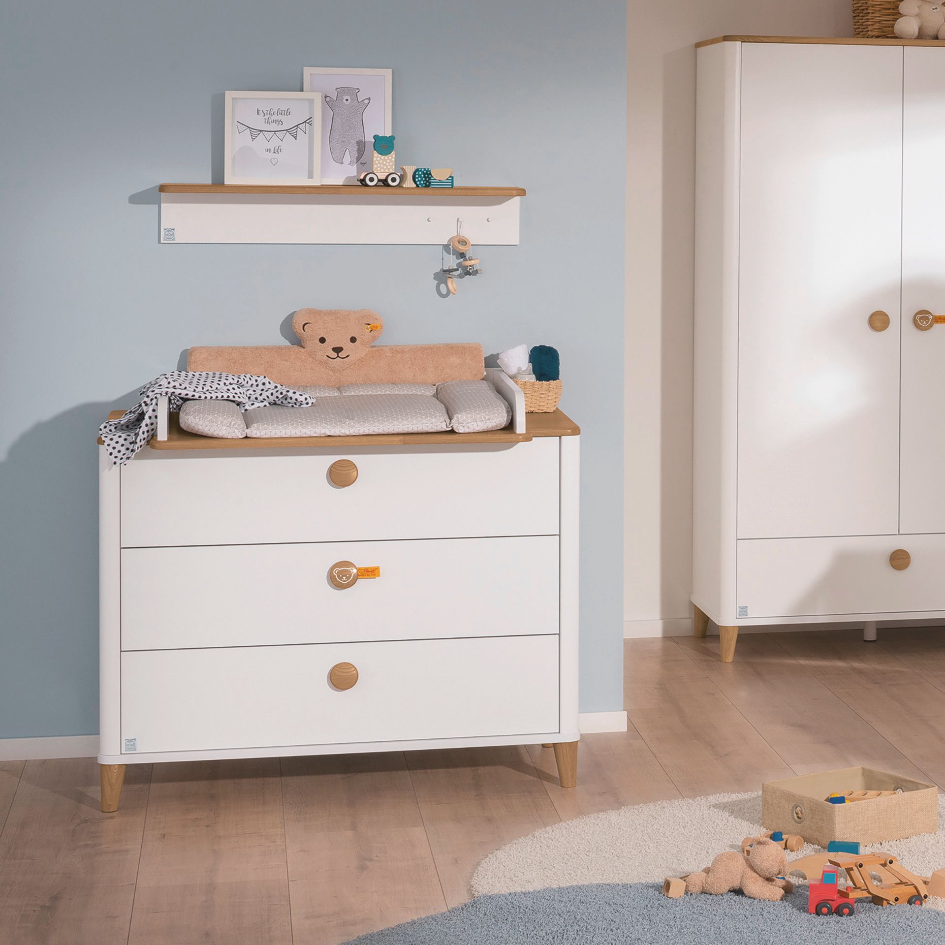 Kopfschutz Steiff by PAIDI Kissen für Wickelaufsatz, Braun Weißer Wickeltisch, Spielzeug und Garderobe in einem gemütlichen Kinderzimmer.