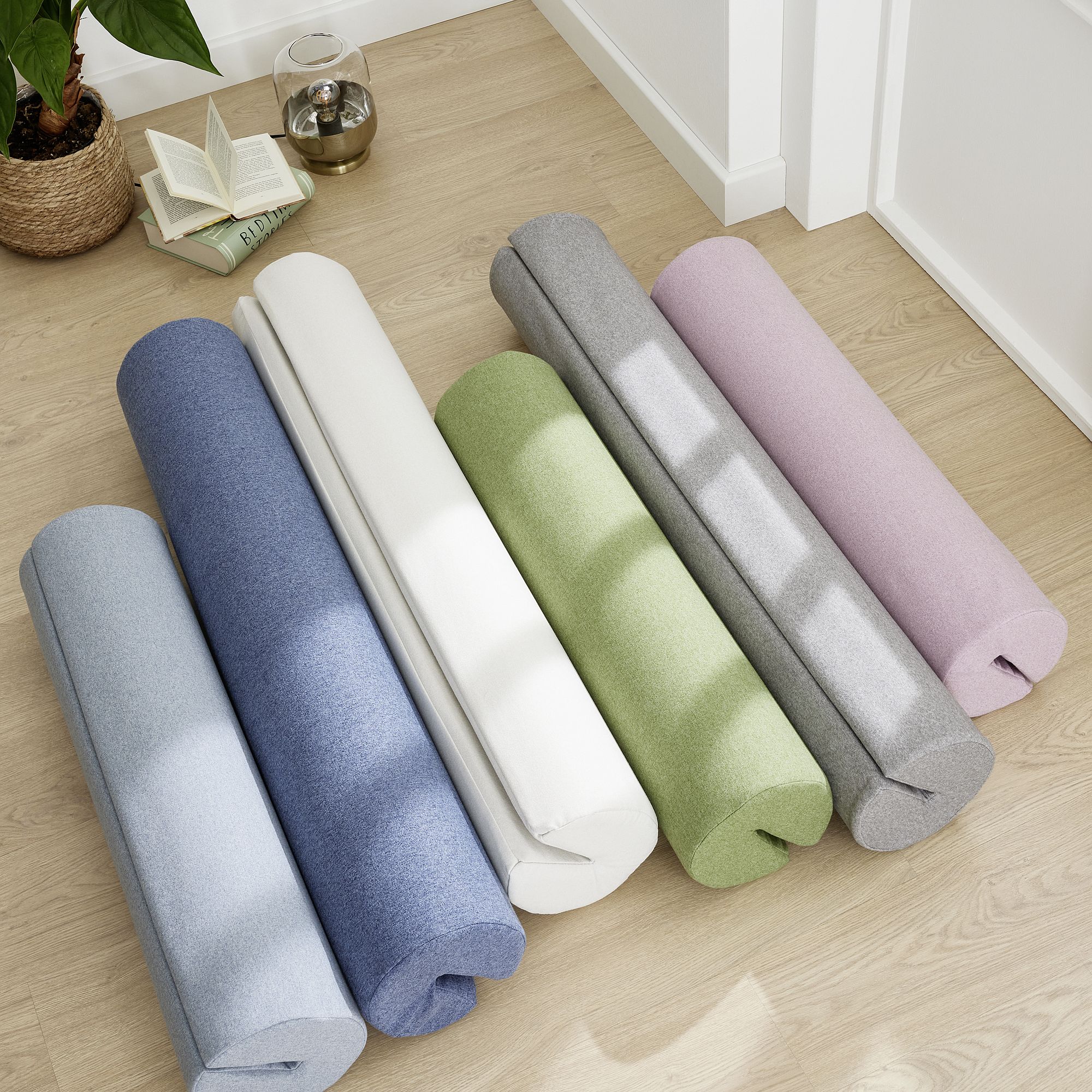 Comfort-Rolle 115 x Ø 20 cm, Mikrofaser Tintenblau Sechs gerollte Yogamatten in Pastellfarben auf einem Holzboden neben einem aufgeschlagenen Buch.