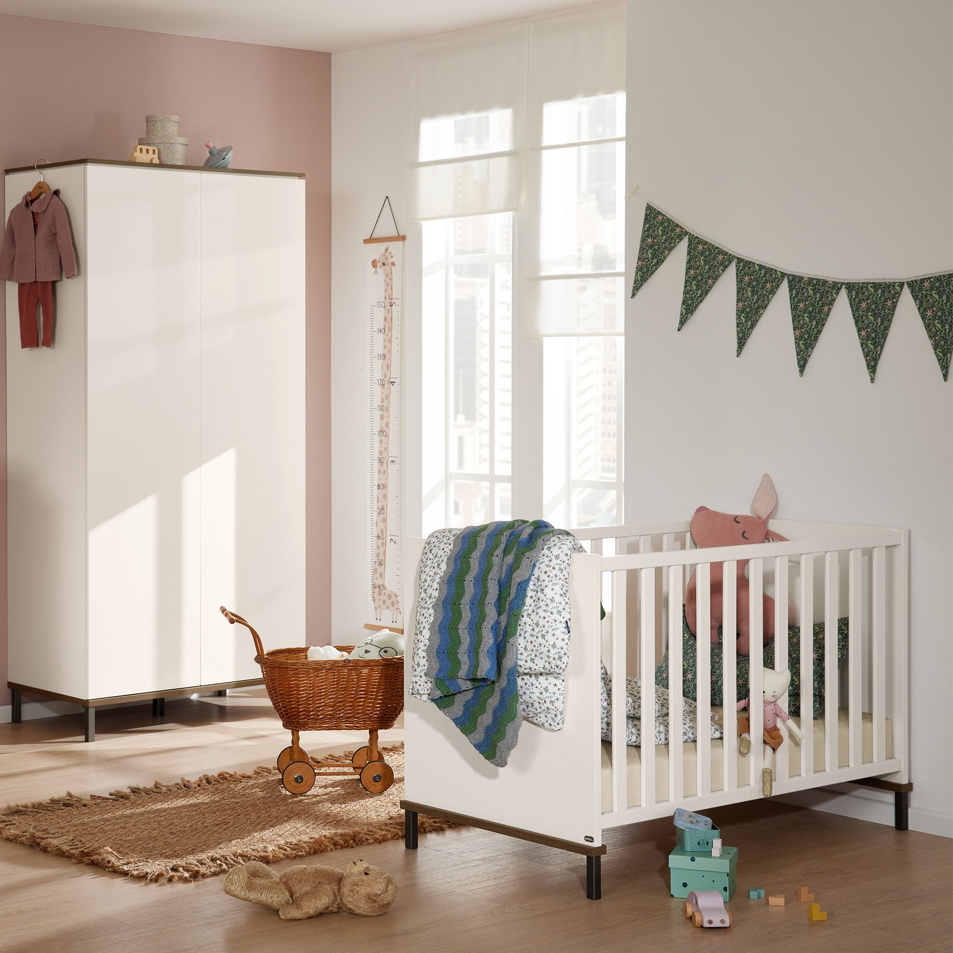 Helles Kinderzimmer mit einem weißen Kinderbett, Spielzeug und einem Korbkinderwagen auf einem gewebten Teppich.