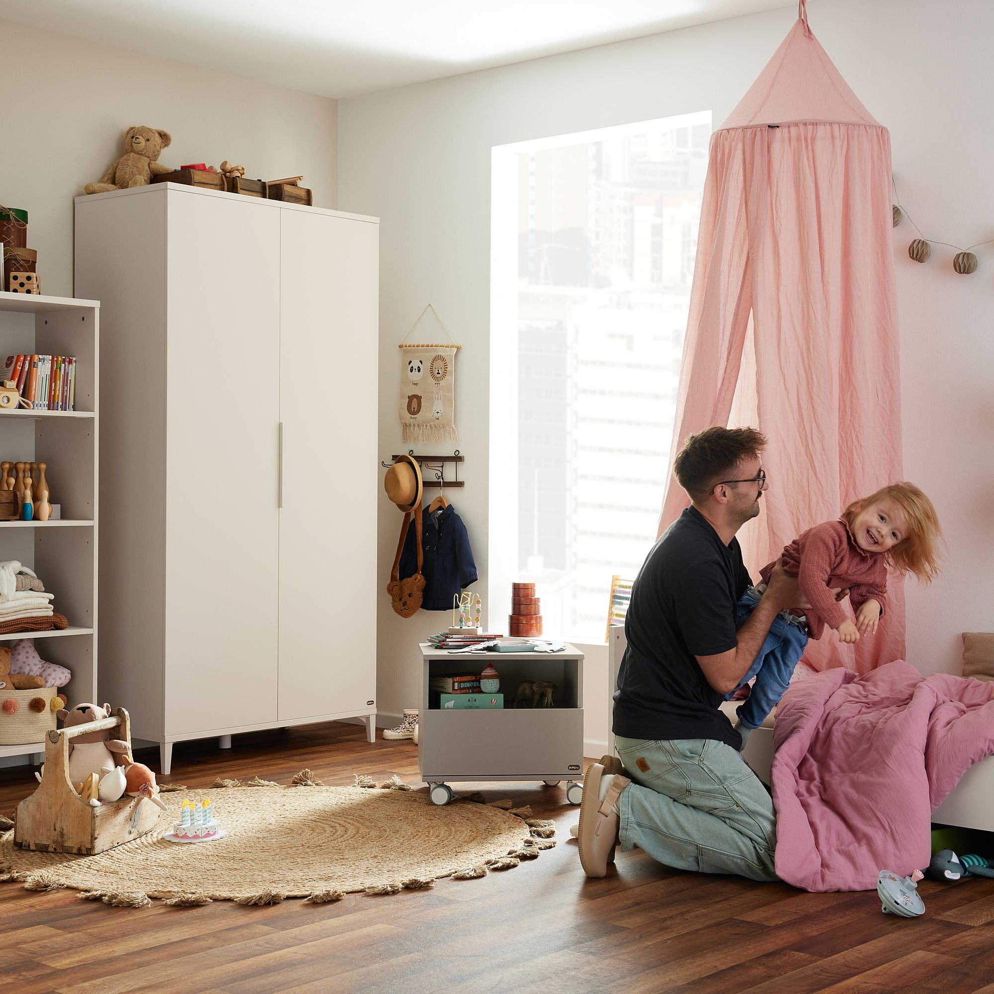 Ein Mann spielt mit einem lächelnden Kind in einem gemütlichen, schön dekorierten Kinderzimmer.