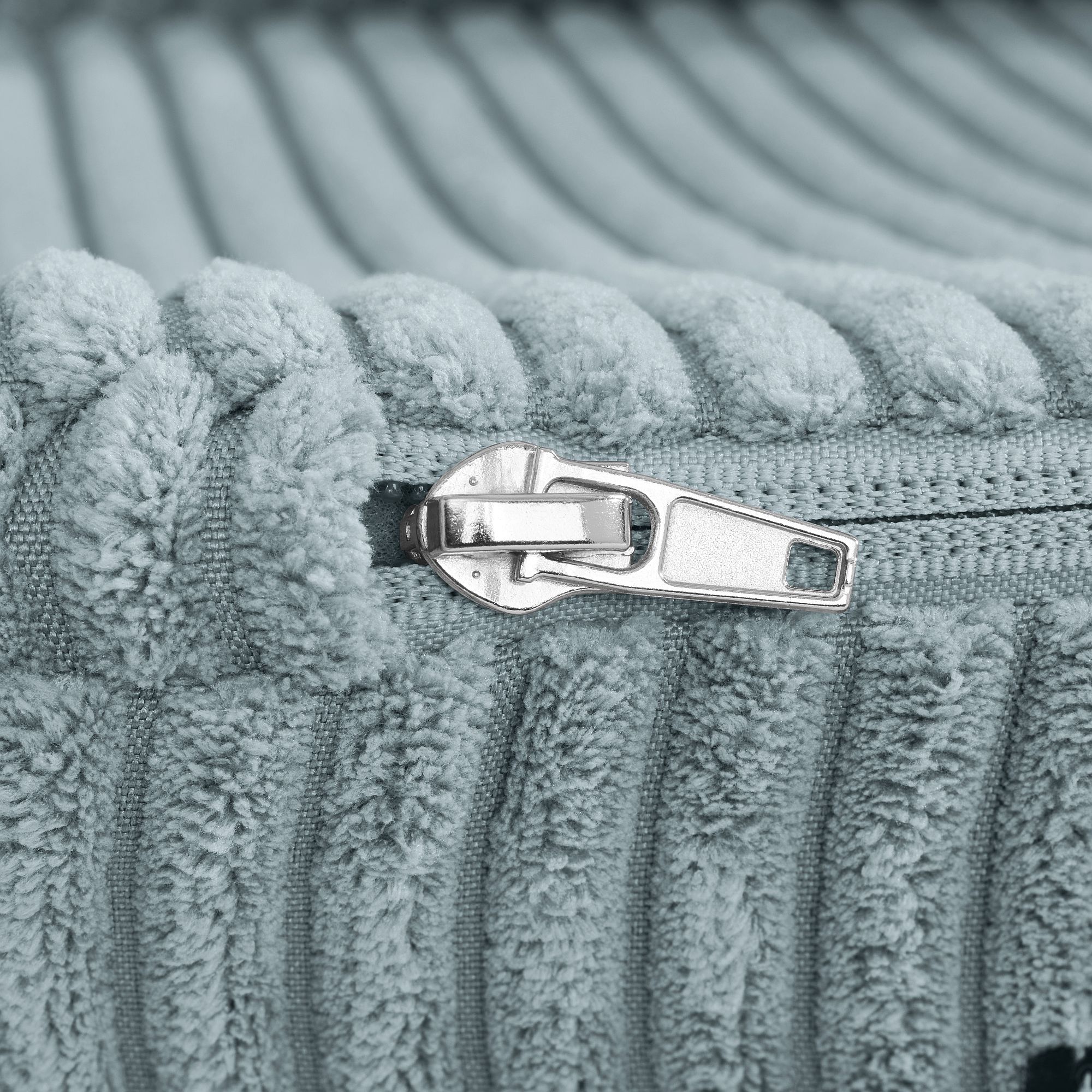 Nahaufnahme eines silbernen Reißverschlusses auf geripptem, hellblauem, strukturiertem Stoff.