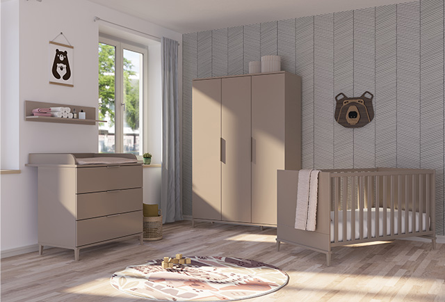 Modernes Kinderzimmer mit beigen Möbeln, einem Kinderbett, einem Kleiderschrank, Schubladen, Wandkunst und einem runden Teppich auf hellem Holzfußboden.