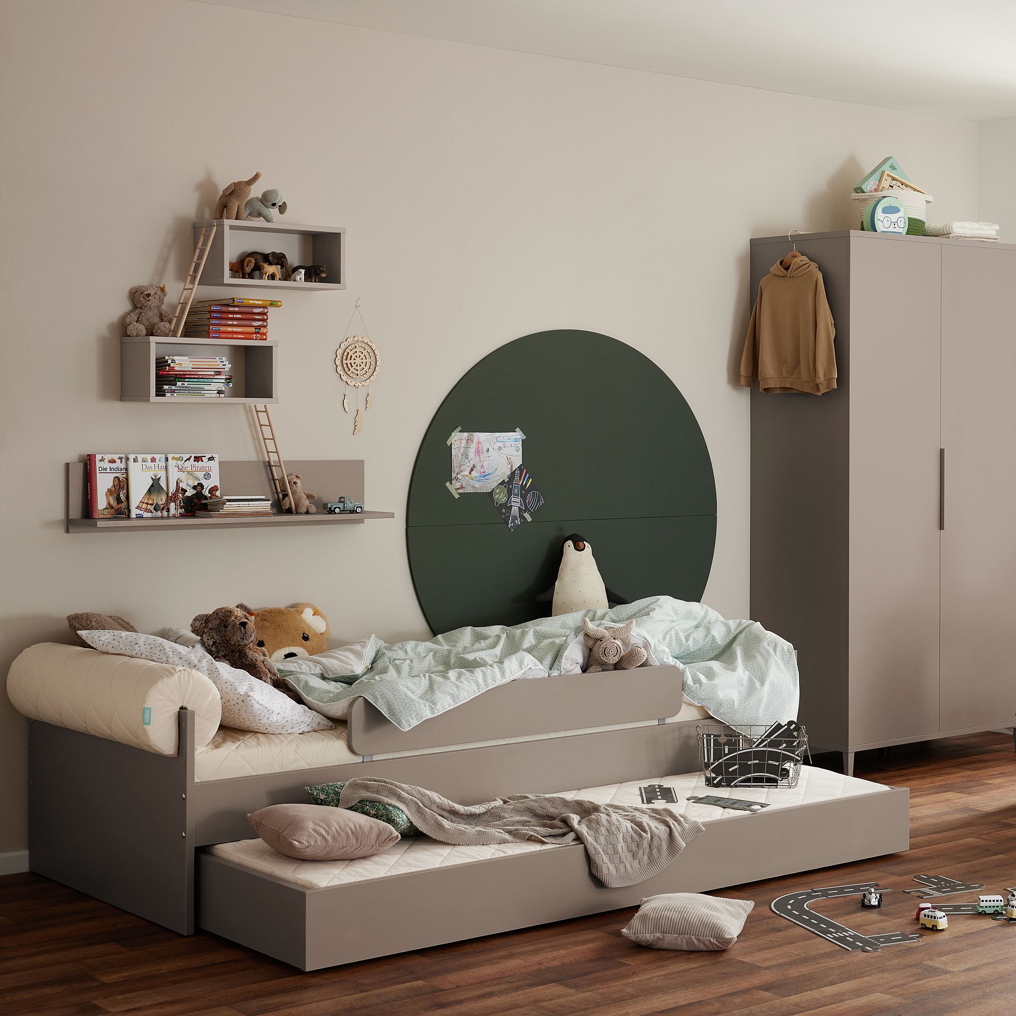 Kinderzimmer mit ausziehbarem Rollbett, Spielzeug, Regalen und einem Kleiderschrank.