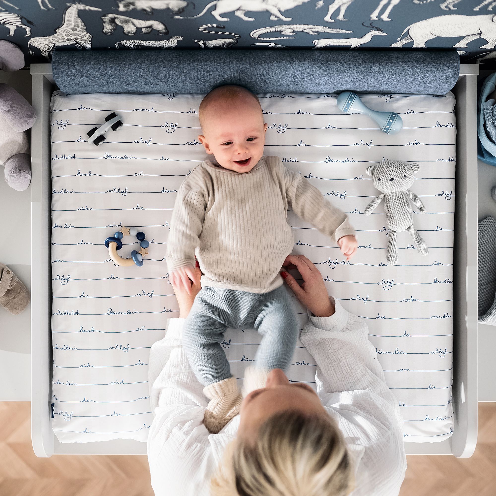 Ein lächelndes Baby liegt auf einer Wickelauflage, während ein Erwachsener seine Taille festhält.