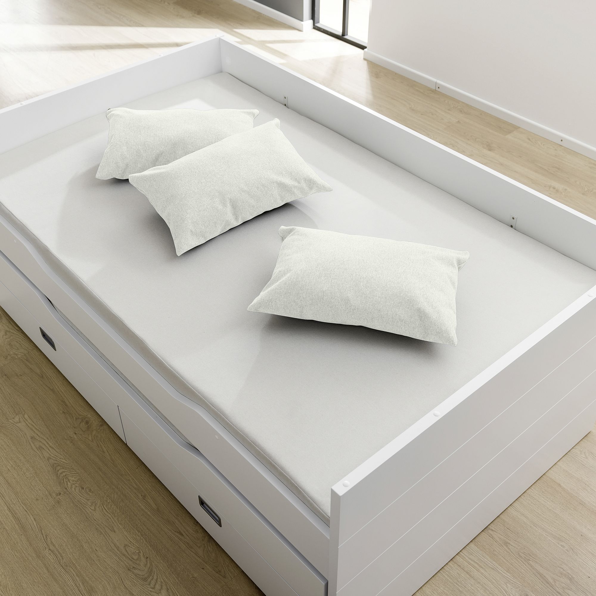 Ein weißes Bett mit drei weißen Kissen in einem hellen, modernen Zimmer mit Holzboden.