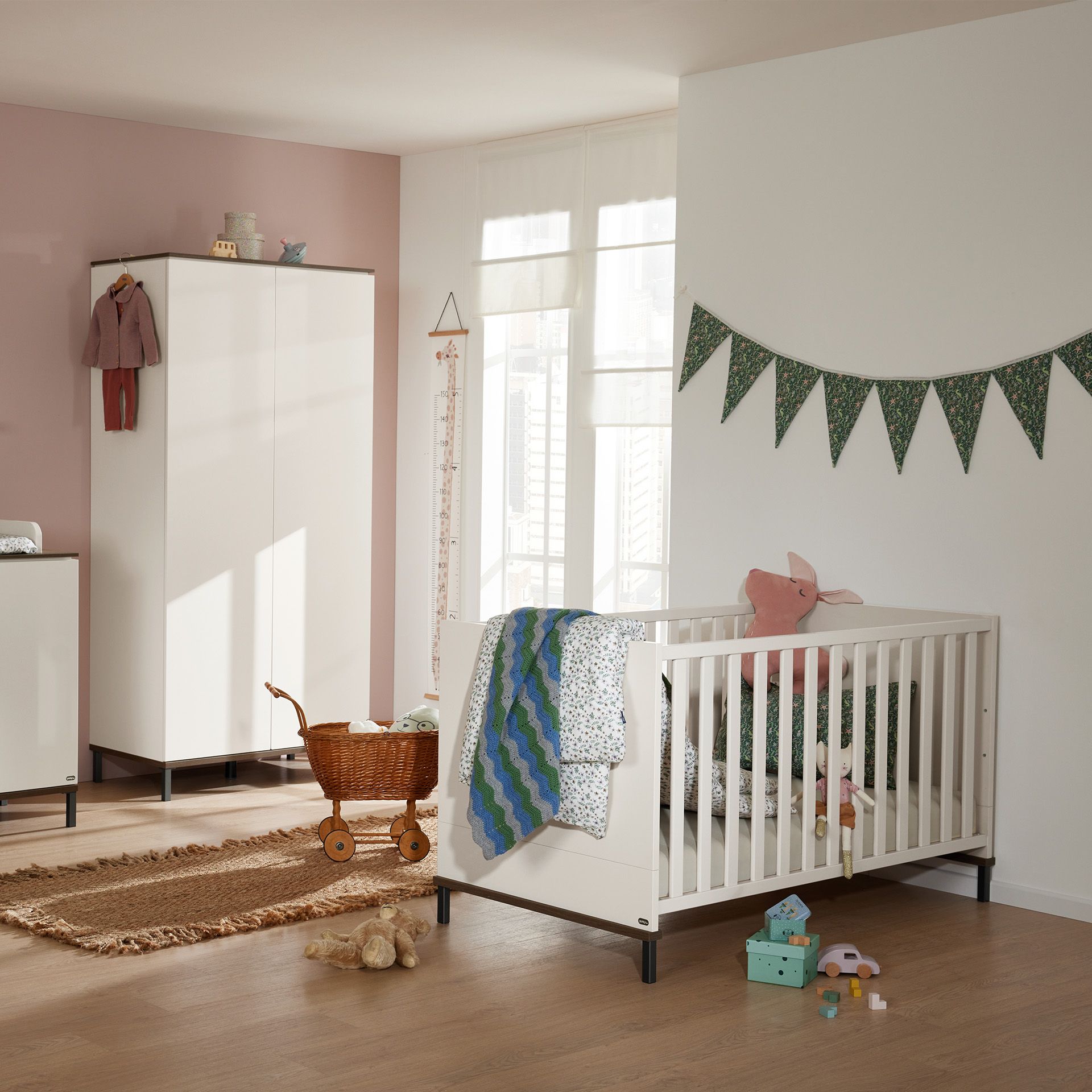 Modernes Kinderzimmer mit weißem Kinderbett, Spielzeug und Girlande an der Wand.