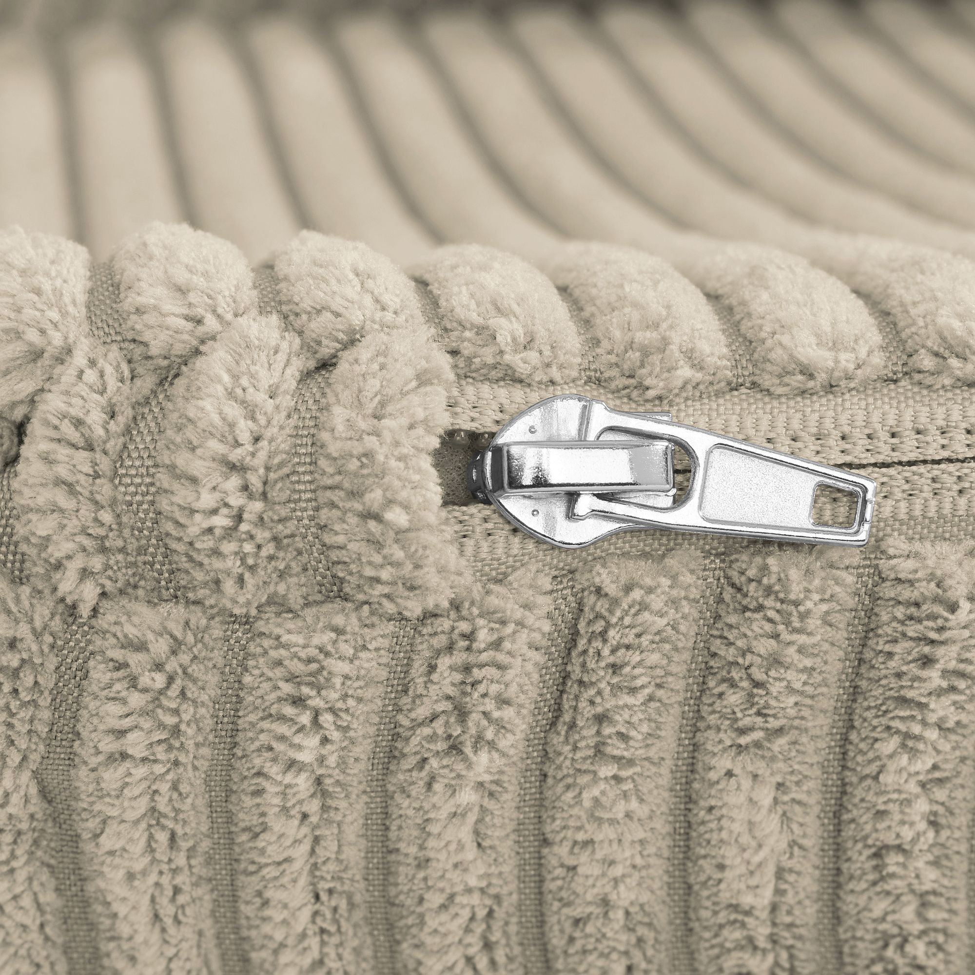 Nahaufnahme eines silbernen Reißverschlusses auf beigefarbenem, geripptem, strukturiertem Stoff.