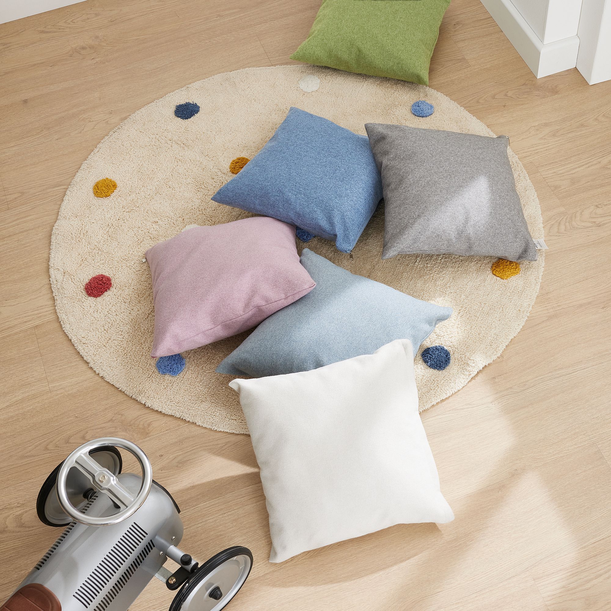 Partykissen 40 x 40 cm, Mikrofaser Dunkelrosa Sechs bunte Kissen auf einem runden Teppich mit Punkten, daneben ein Spielzeugauto auf Holzboden.