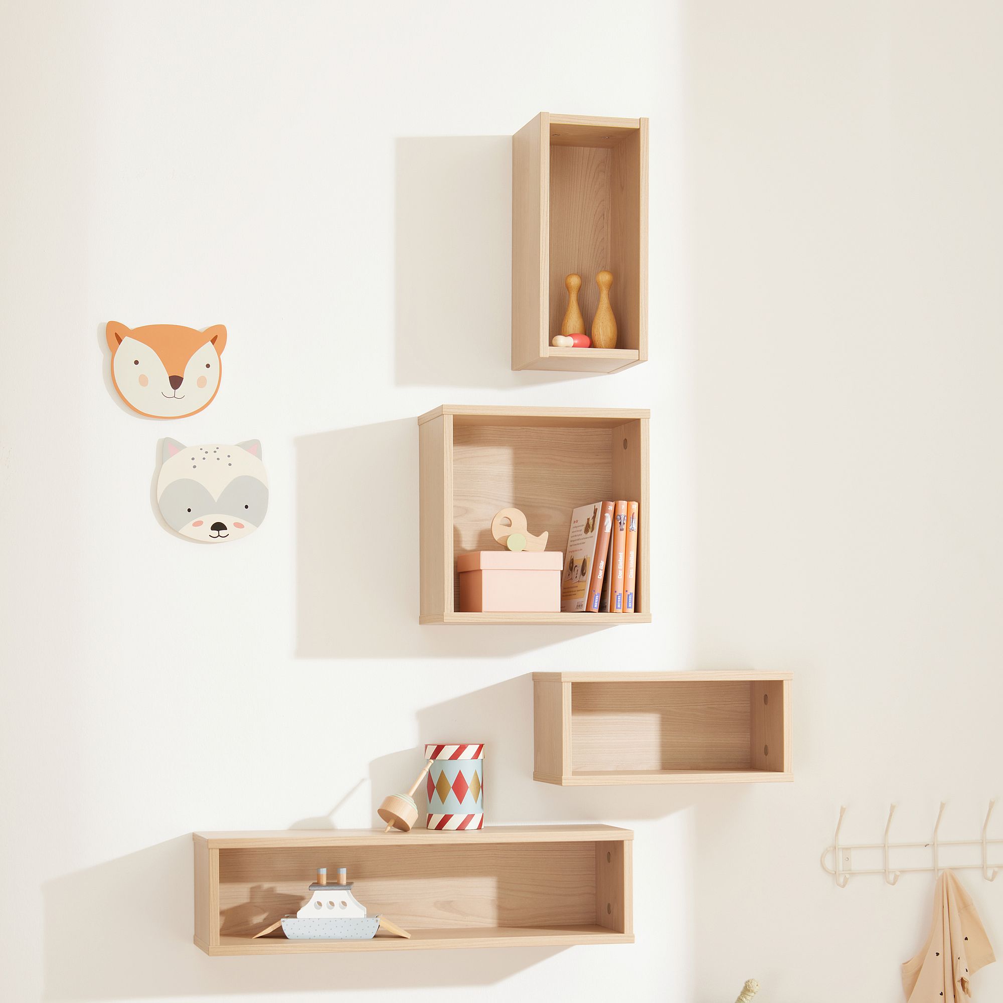 Helle Holzregale mit Spielzeug und Tierdekor an einer weißen Wand.
