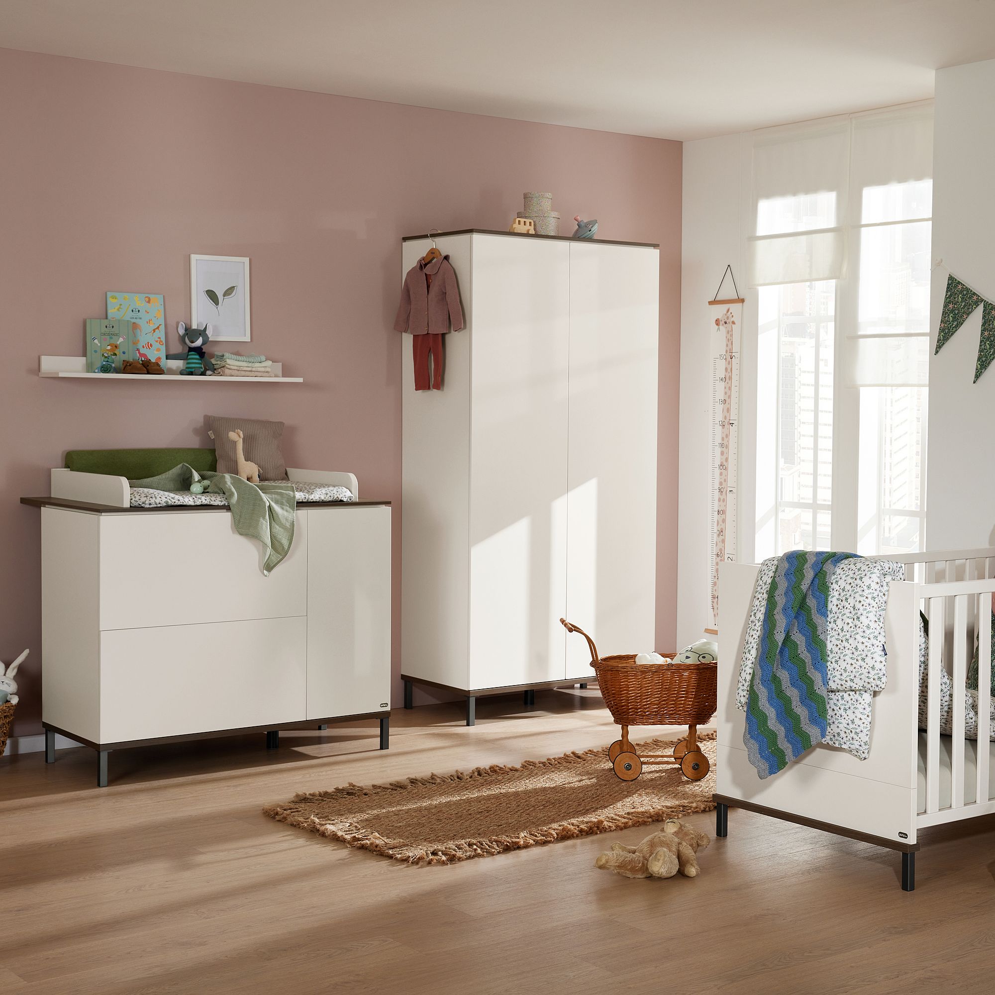 Modernes Kinderzimmer mit weißen Möbeln, Kinderbett, Korbwagen und rosa Akzentwand.
