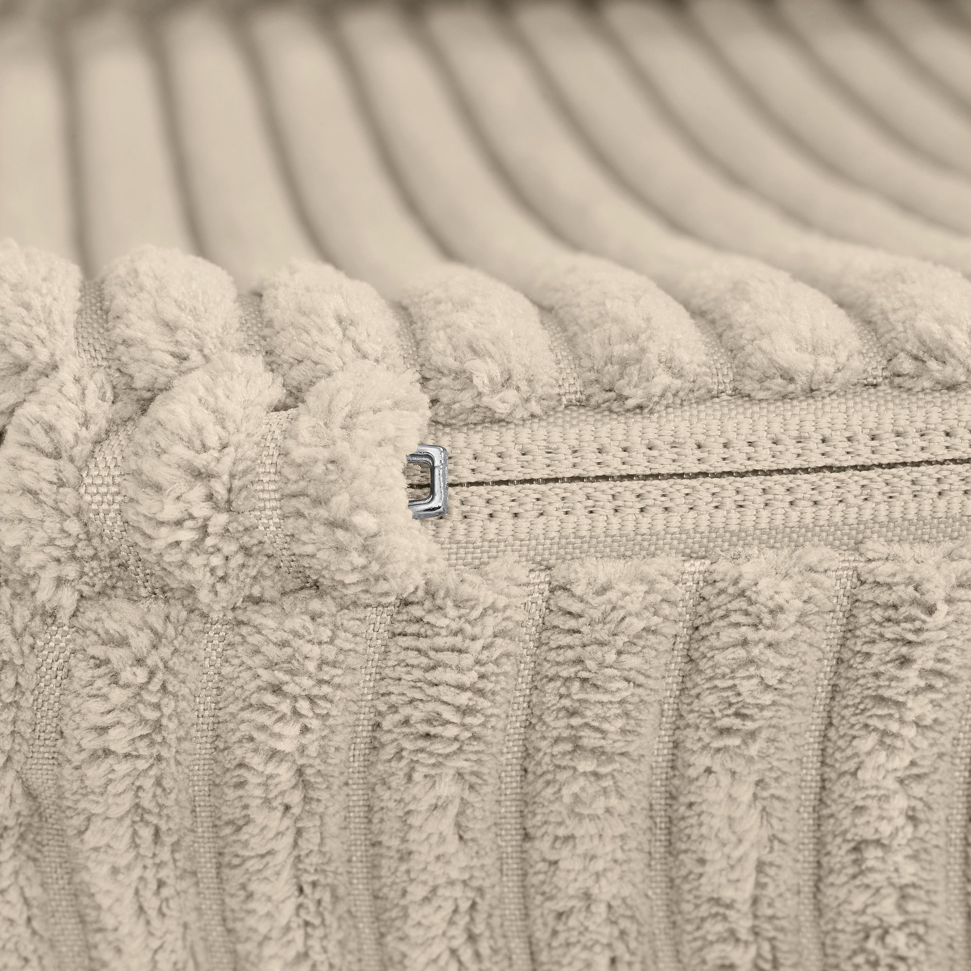 Nahaufnahme eines beigen Rippenstoffkissens mit sichtbarem Reißverschluss.